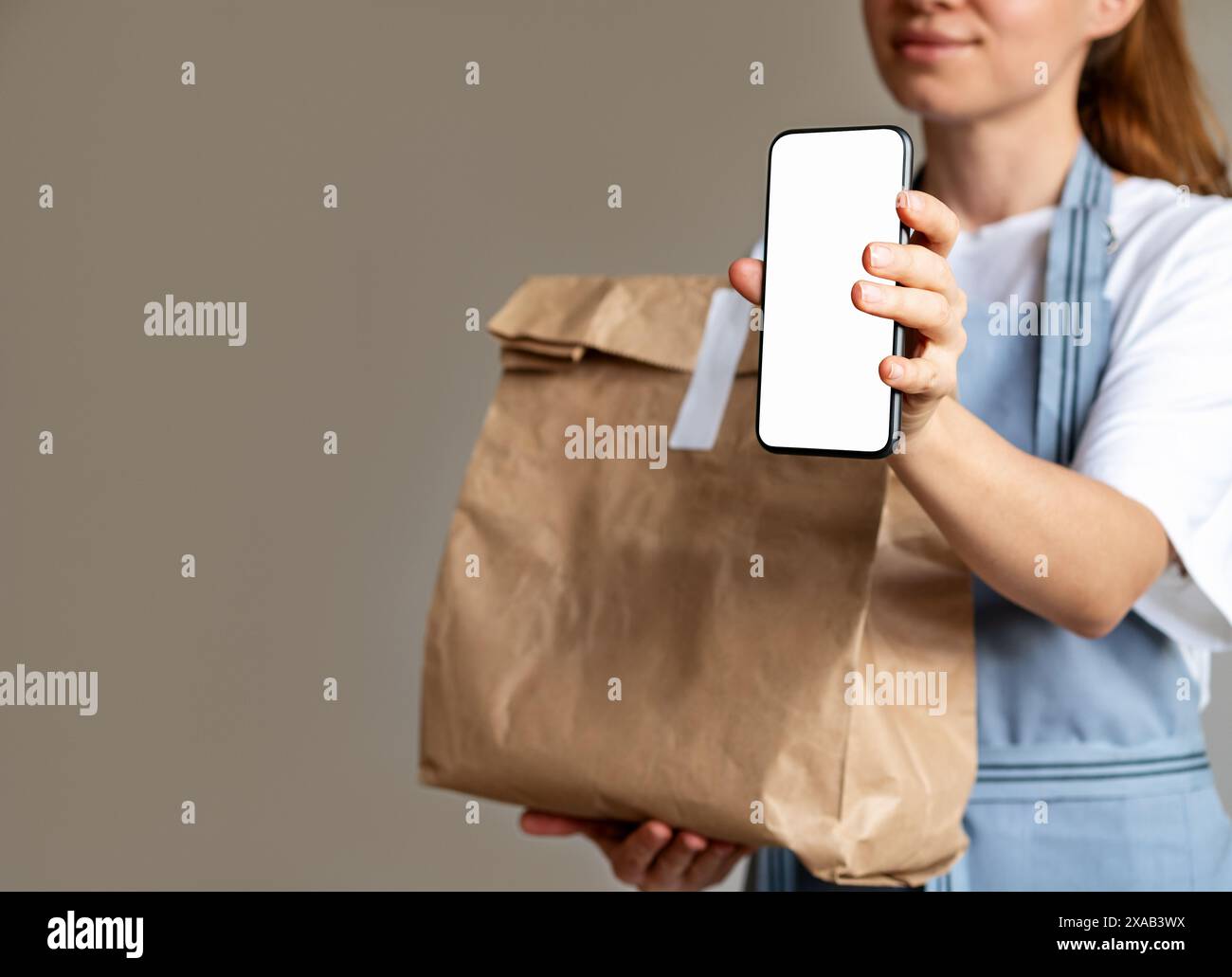 Service mobile de livraison de nourriture. Smartphone avec écran vierge et sac alimentaire brun dans les mains de la personne féminine. Banque D'Images