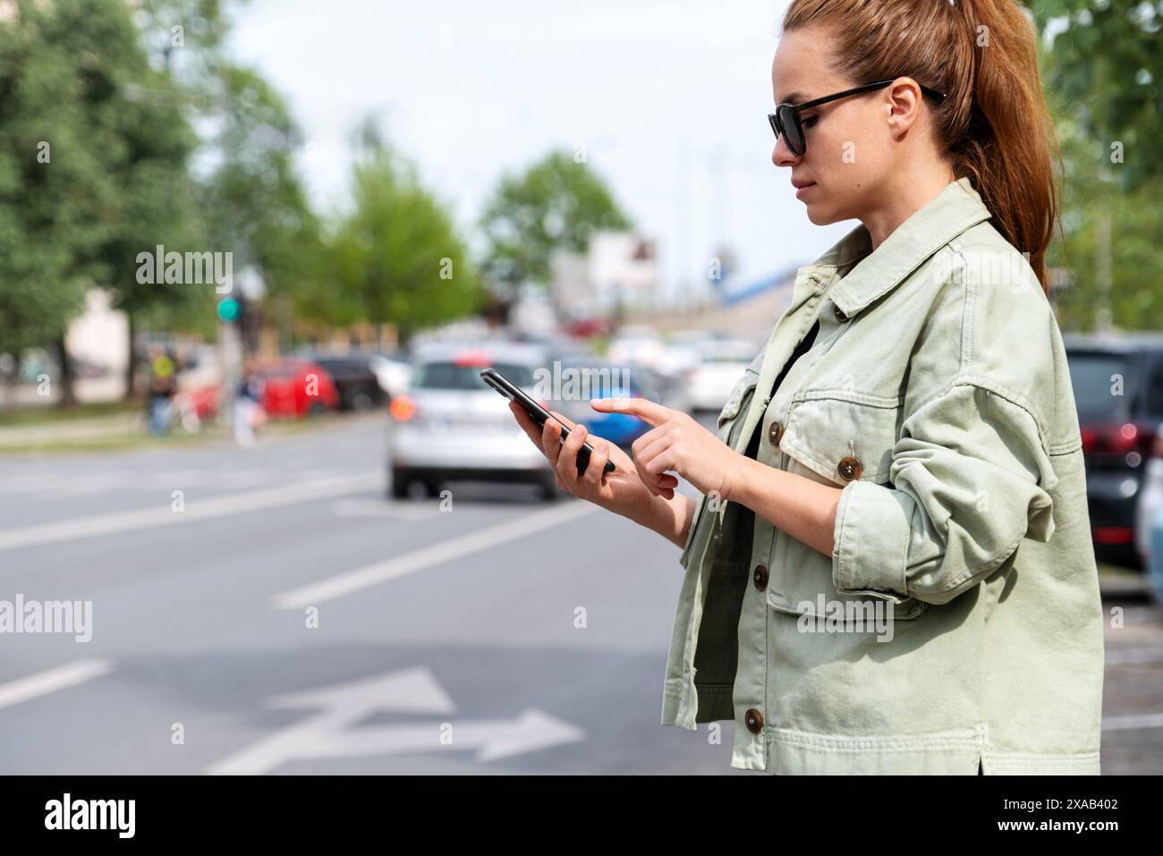 Service de voiture de dépannage. Femme urbaine portant des lunettes de soleil se tient à côté de la route de la ville et la réservation d'un taxi en ligne à l'aide d'un smartphone. Banque D'Images