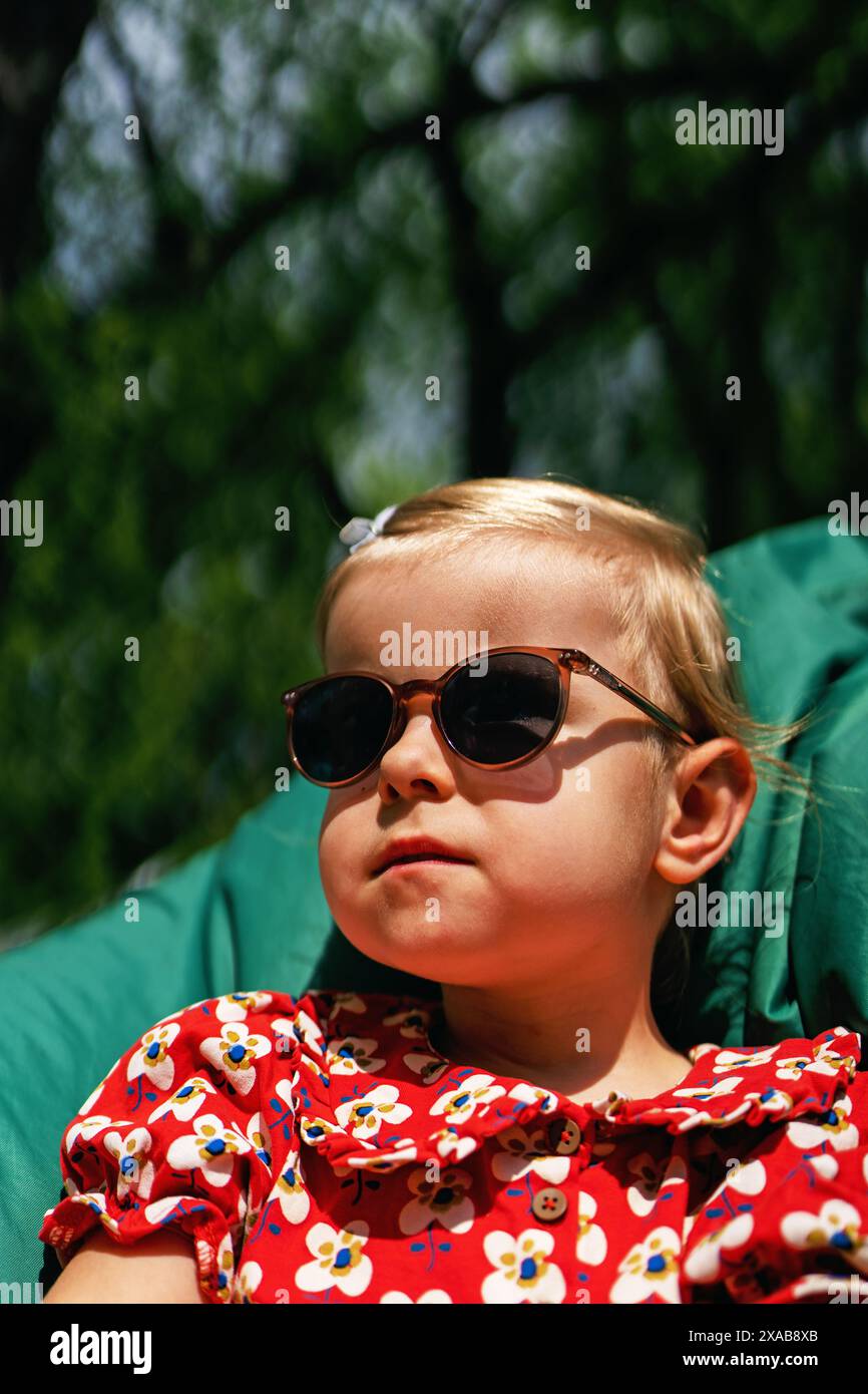 Portrait d'une belle petite fille à la mode et élégante dans des lunettes de soleil et une robe rouge. Banque D'Images