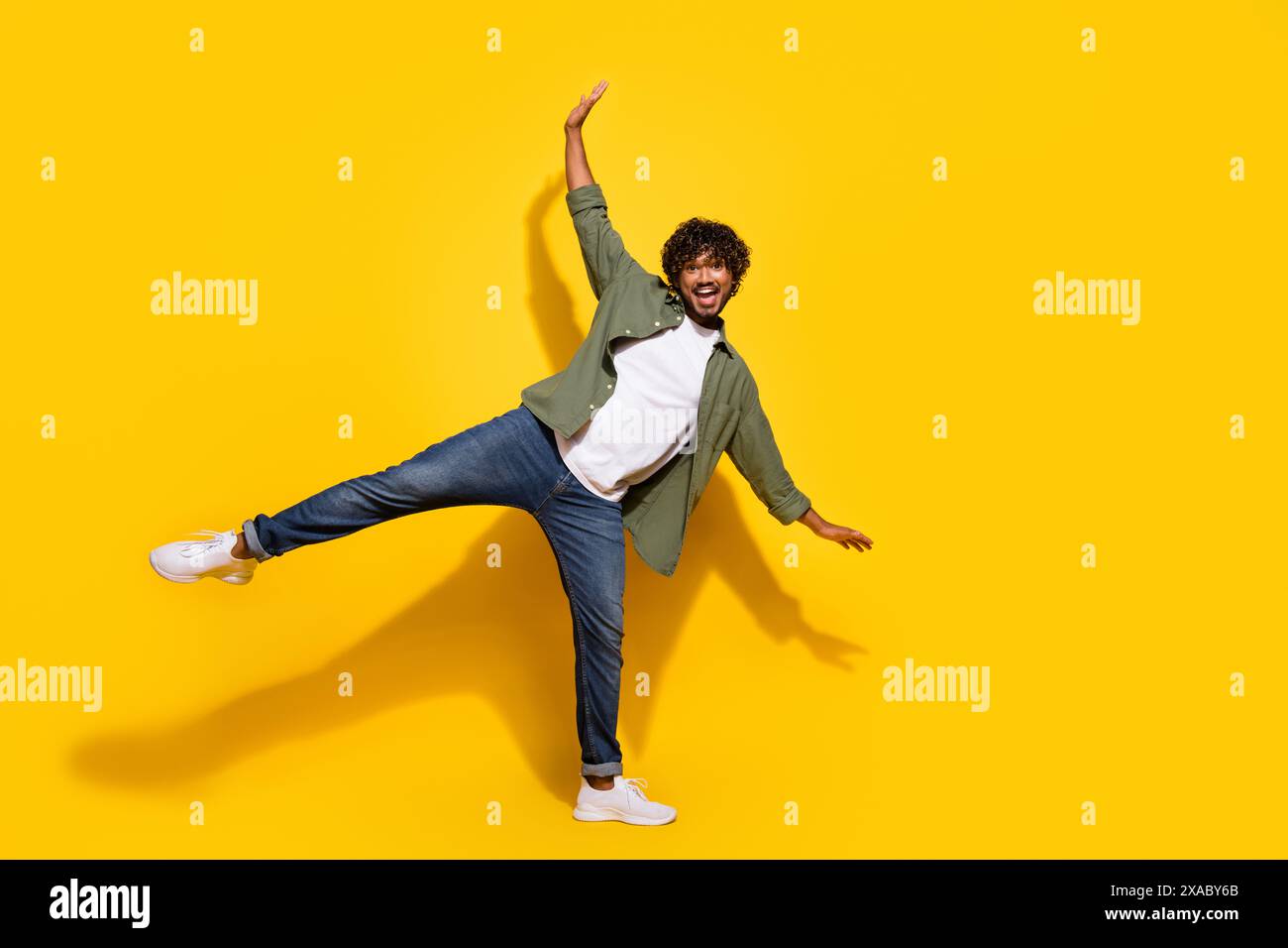 Photo de portrait du jeune mec mexicain drôle en chemise kaki et jeans debout garder l'équilibre isolé sur fond de couleur jaune Banque D'Images