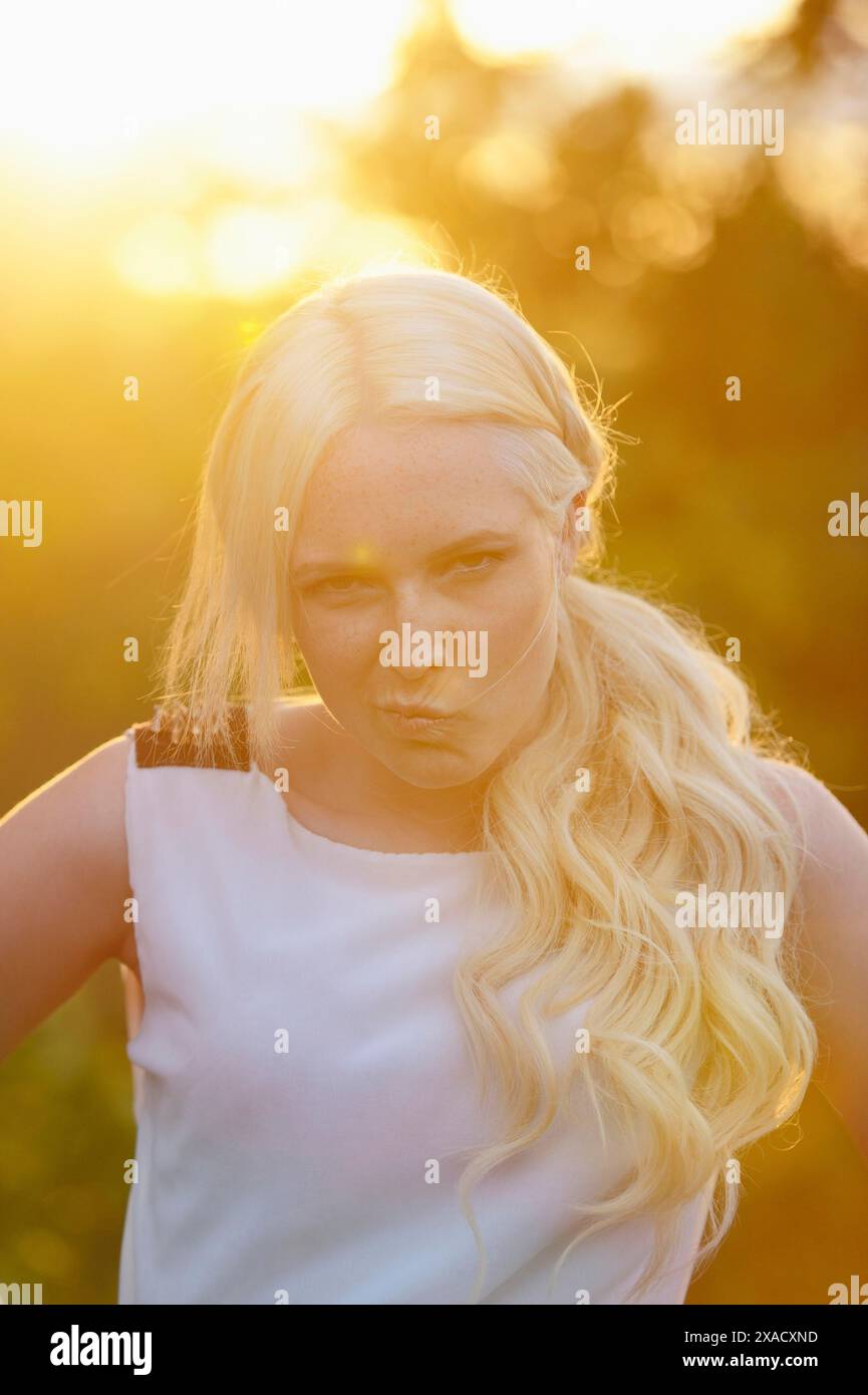 Une femme aux cheveux blonds pose à la lumière du soleil du soir, portant une robe blanche dans un cadre extérieur Banque D'Images