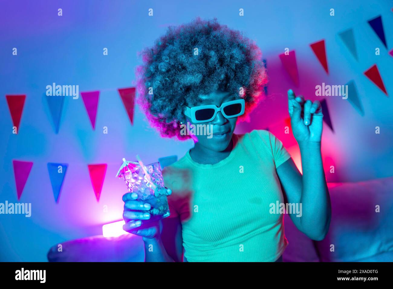 Femme africaine cool avec des lunettes de soleil dansant, buvant un cocktail et faisant la fête à la maison Banque D'Images