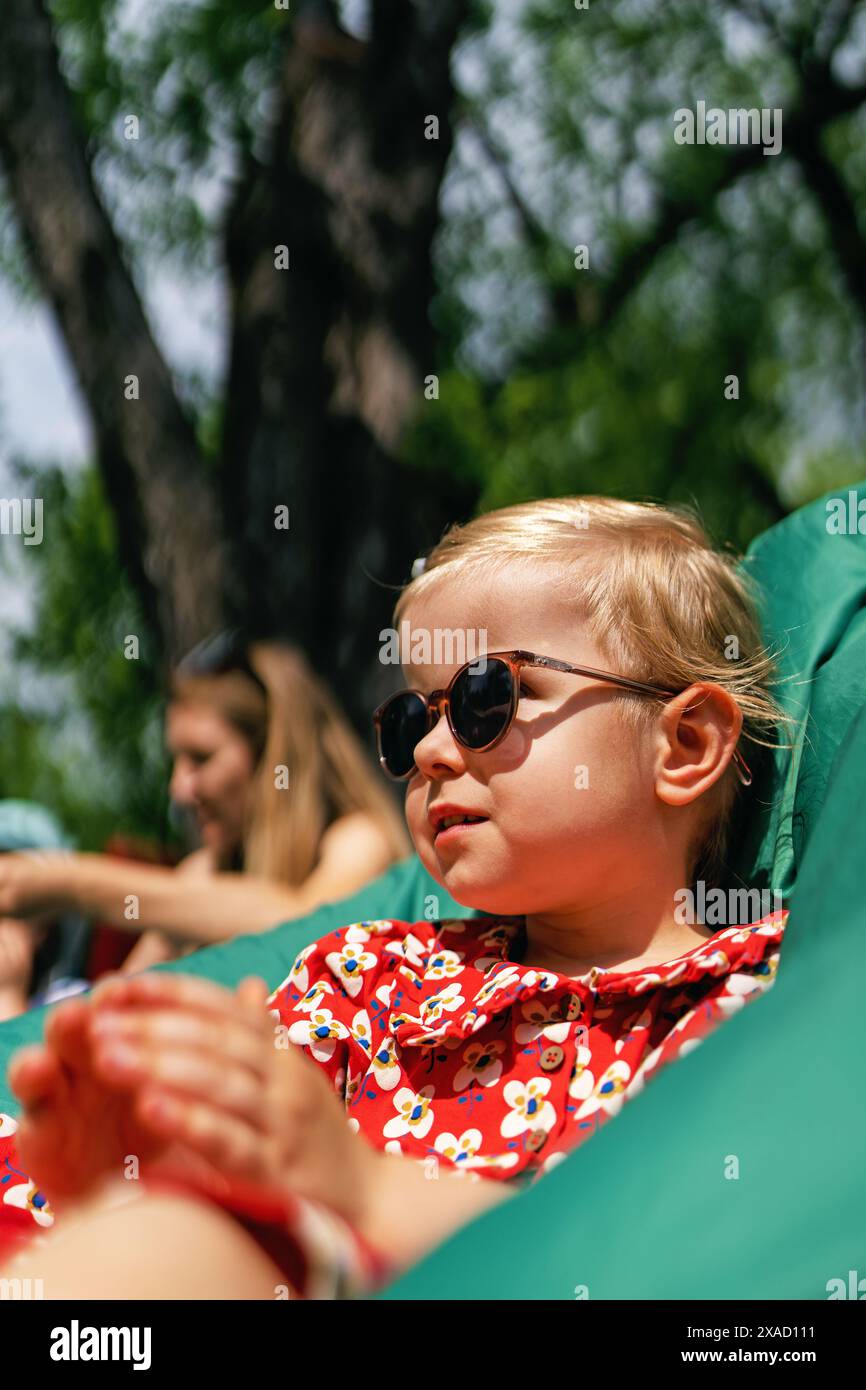 Portrait d'une belle petite fille à la mode et élégante dans des lunettes de soleil et une robe rouge. Banque D'Images