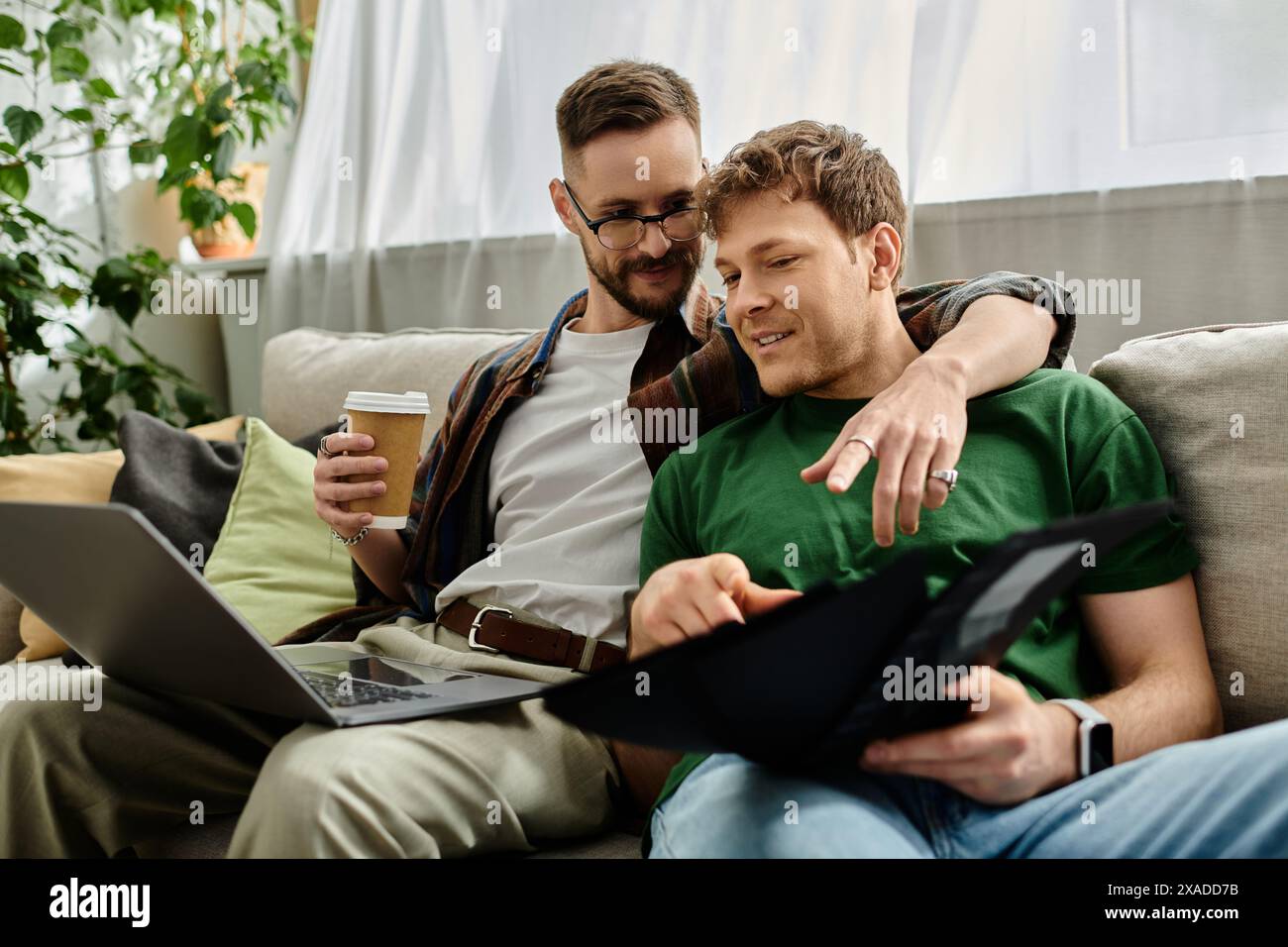 Deux hommes amoureux, assis sur un canapé, travaillant ensemble sur un ordinateur portable dans leur atelier de designer. Banque D'Images