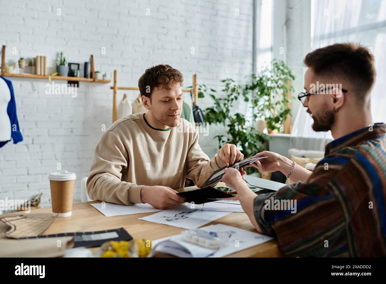 Deux hommes travaillant ensemble sur un design de vêtements tendance dans un atelier de designer. Banque D'Images