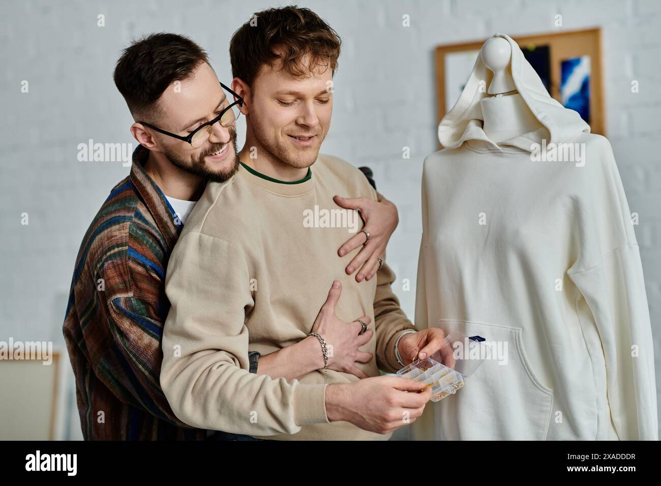 Un couple gay se tient côte à côte dans un atelier de designer, travaillant ensemble sur des vêtements tendance. Banque D'Images
