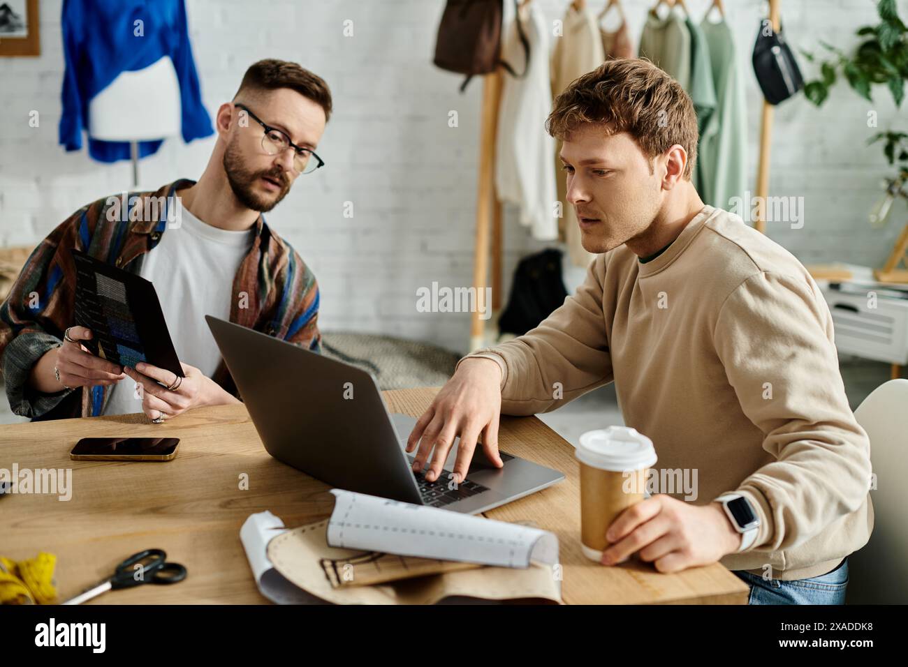 Deux hommes, un couple gay, sont assis à une table travaillant ensemble sur un ordinateur portable dans un atelier de designer. Banque D'Images