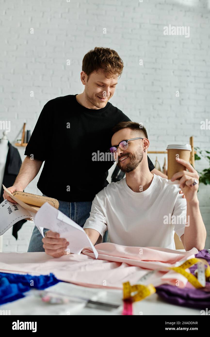Deux hommes amoureux, collaborant de manière créative autour d'un morceau de papier à une table élégante. Banque D'Images