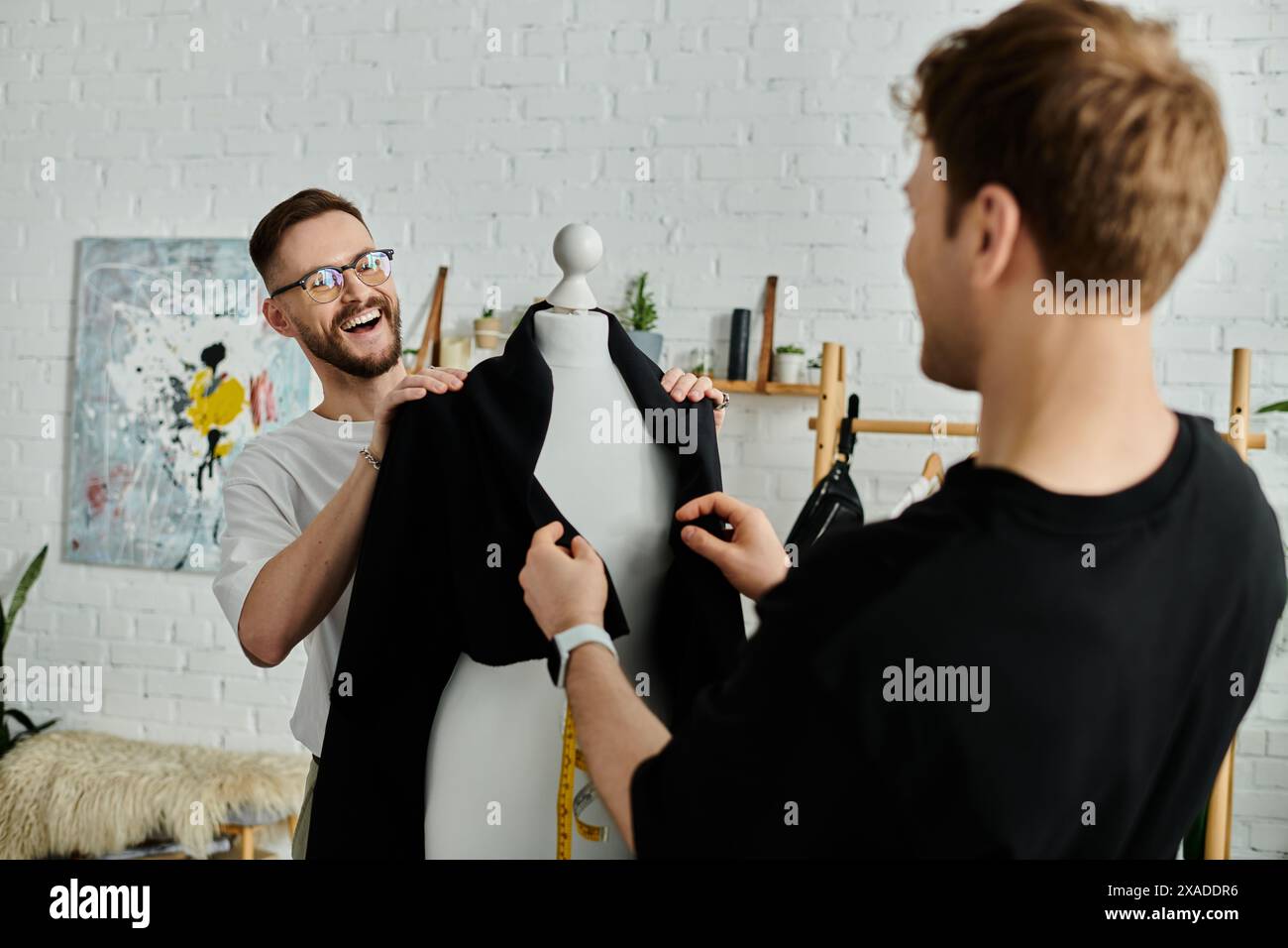 Un homme et un mannequin tiennent une chemise noire, travaillant dans un atelier de designer. Banque D'Images