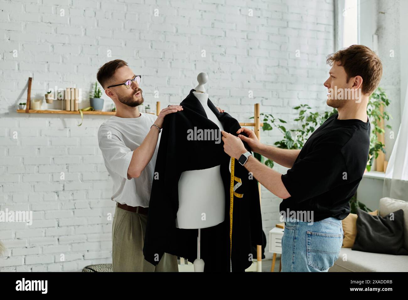 Deux hommes, designers, se tiennent unis dans un atelier créatif, travaillant ensemble sur des vêtements tendance. Banque D'Images