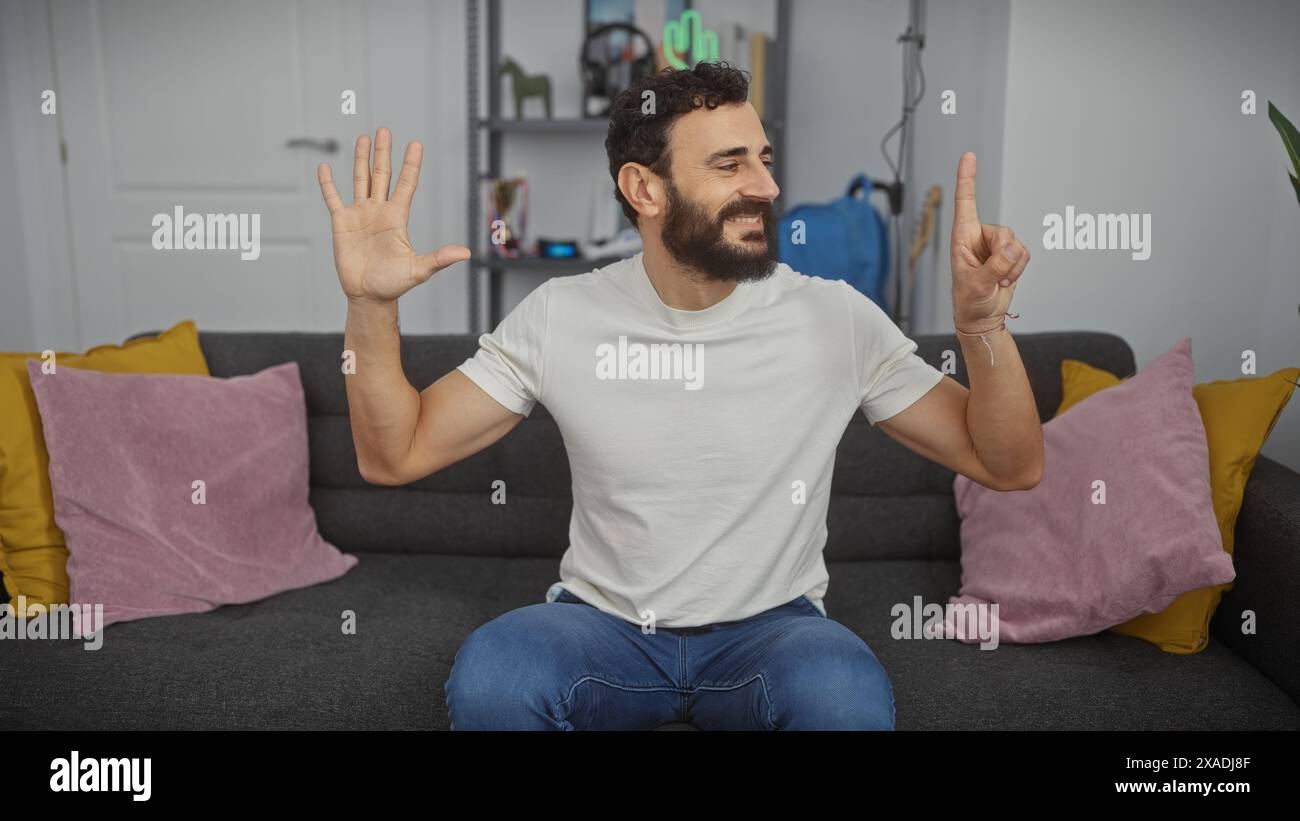 Un homme joyeux affichant six doigts à l'intérieur avec une tenue décontractée et un décor de salon confortable en arrière-plan. Banque D'Images