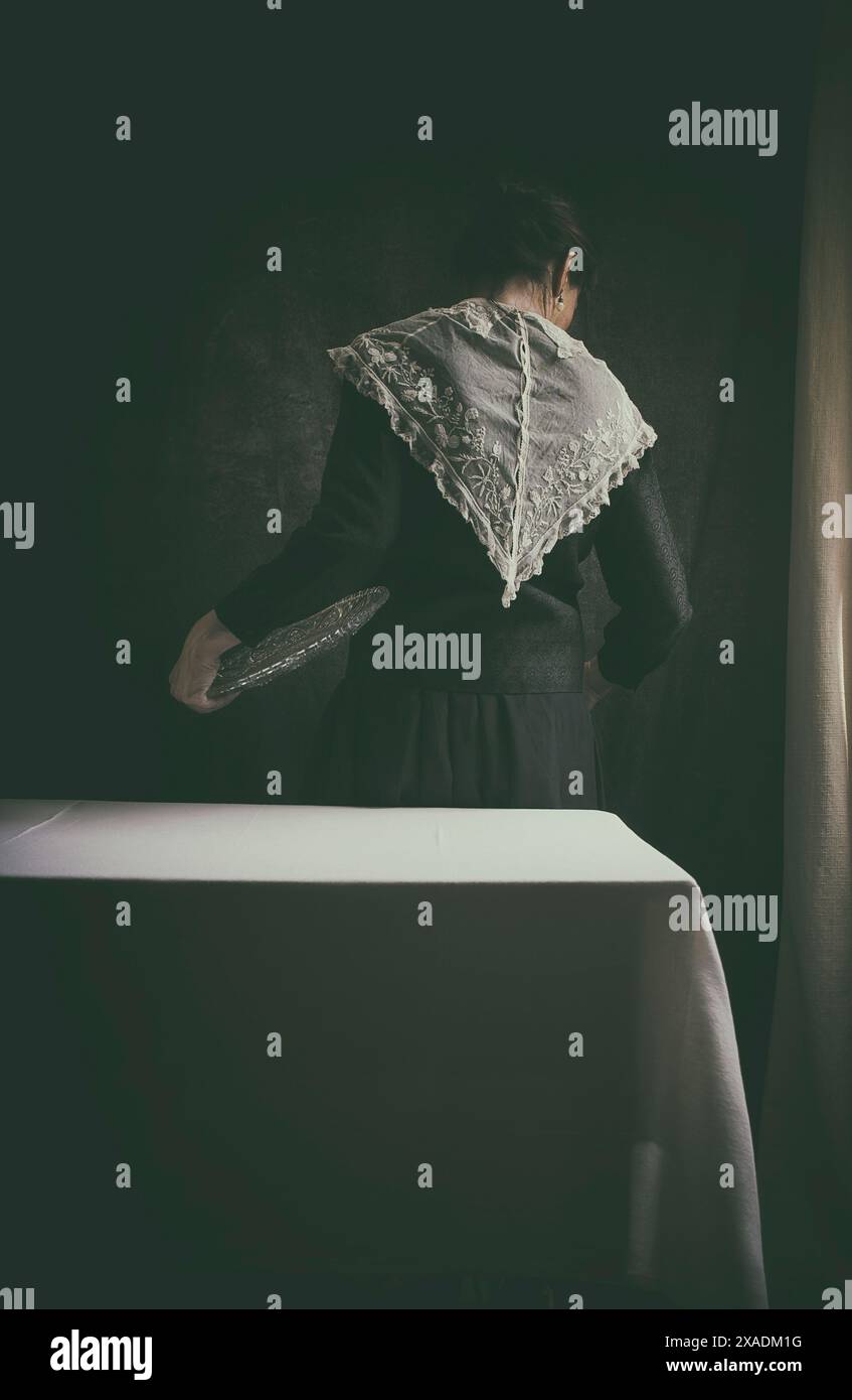 Femme au style édouardien et collier en dentelle dans une scène domestique derrière une table avec une nappe en lin blanc, une scène qui réinterprète le style de th Banque D'Images