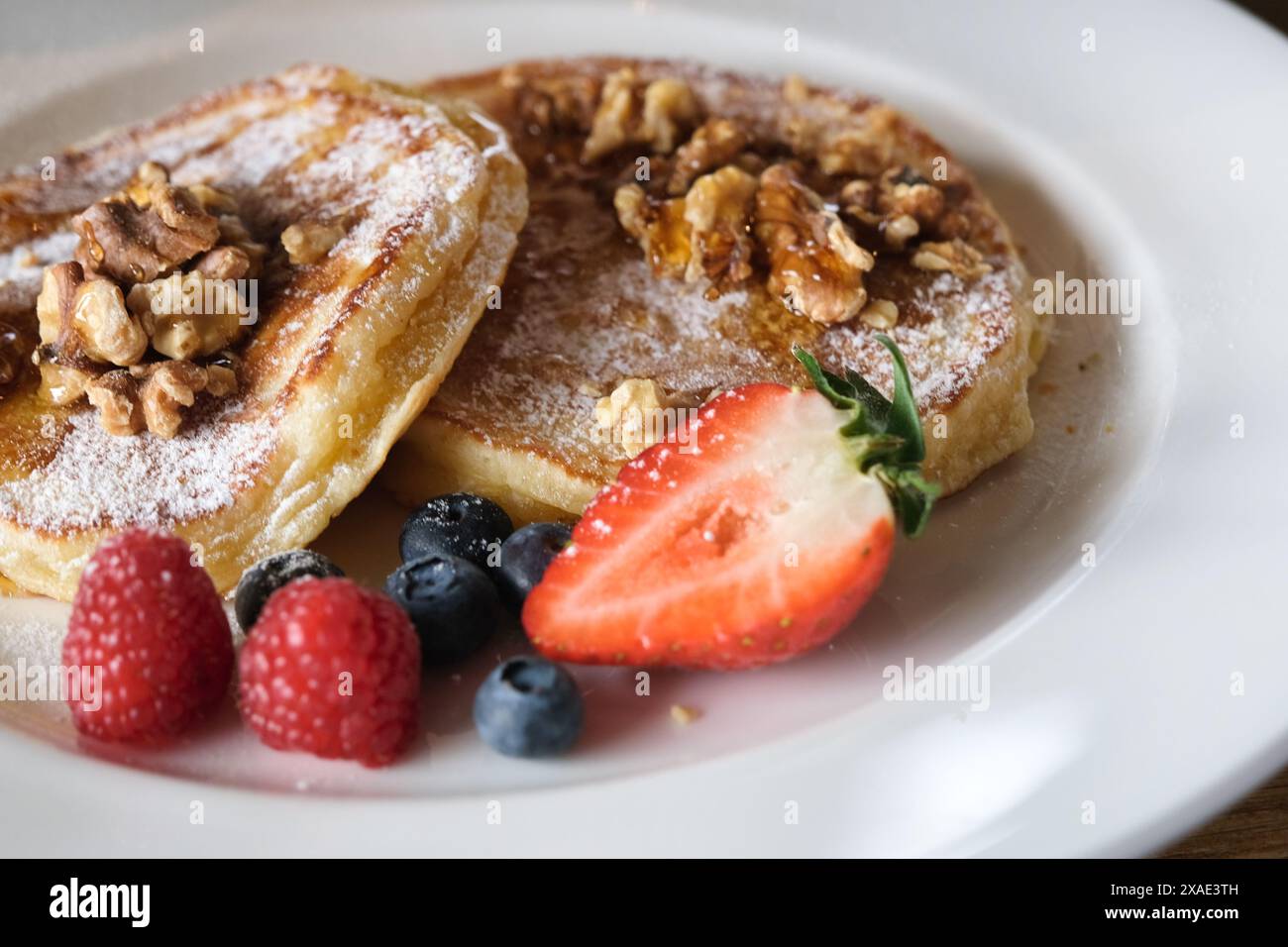 Une assiette de crêpes avec des myrtilles et des fraises sur le dessus. L'assiette est blanche et la nourriture est colorée Banque D'Images