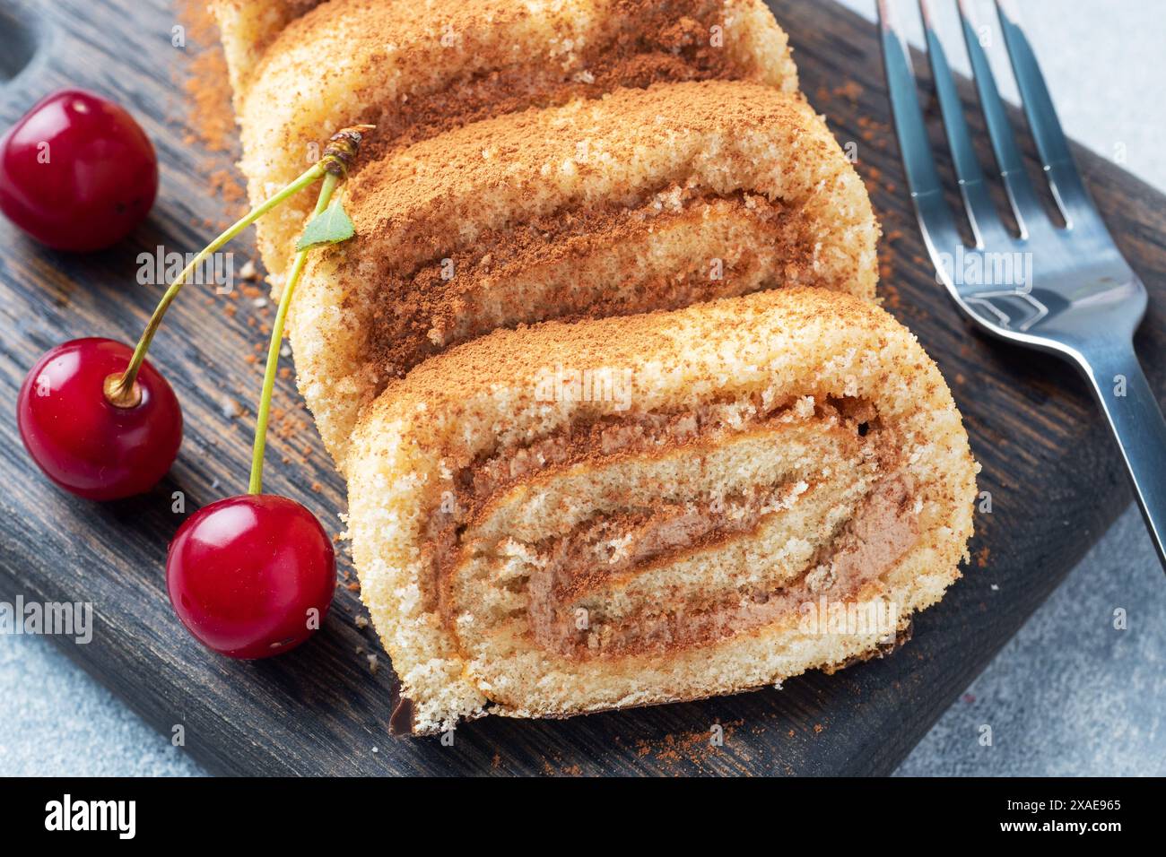 Dessert rouleau éponge avec crème au chocolat avec cerises sur une planche à découper en bois Banque D'Images Dessert rouleau éponge avec crème au chocolat avec cerises sur une planche à découper en bois Banque D'Images
