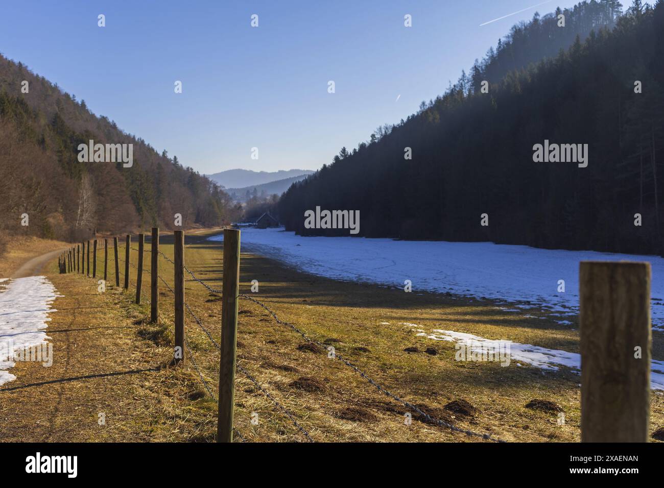 Photographie panoramique d'une vallée alpine avec clôture au premier plan et ferme dans la distance le jour ensoleillé d'hiver Banque D'Images