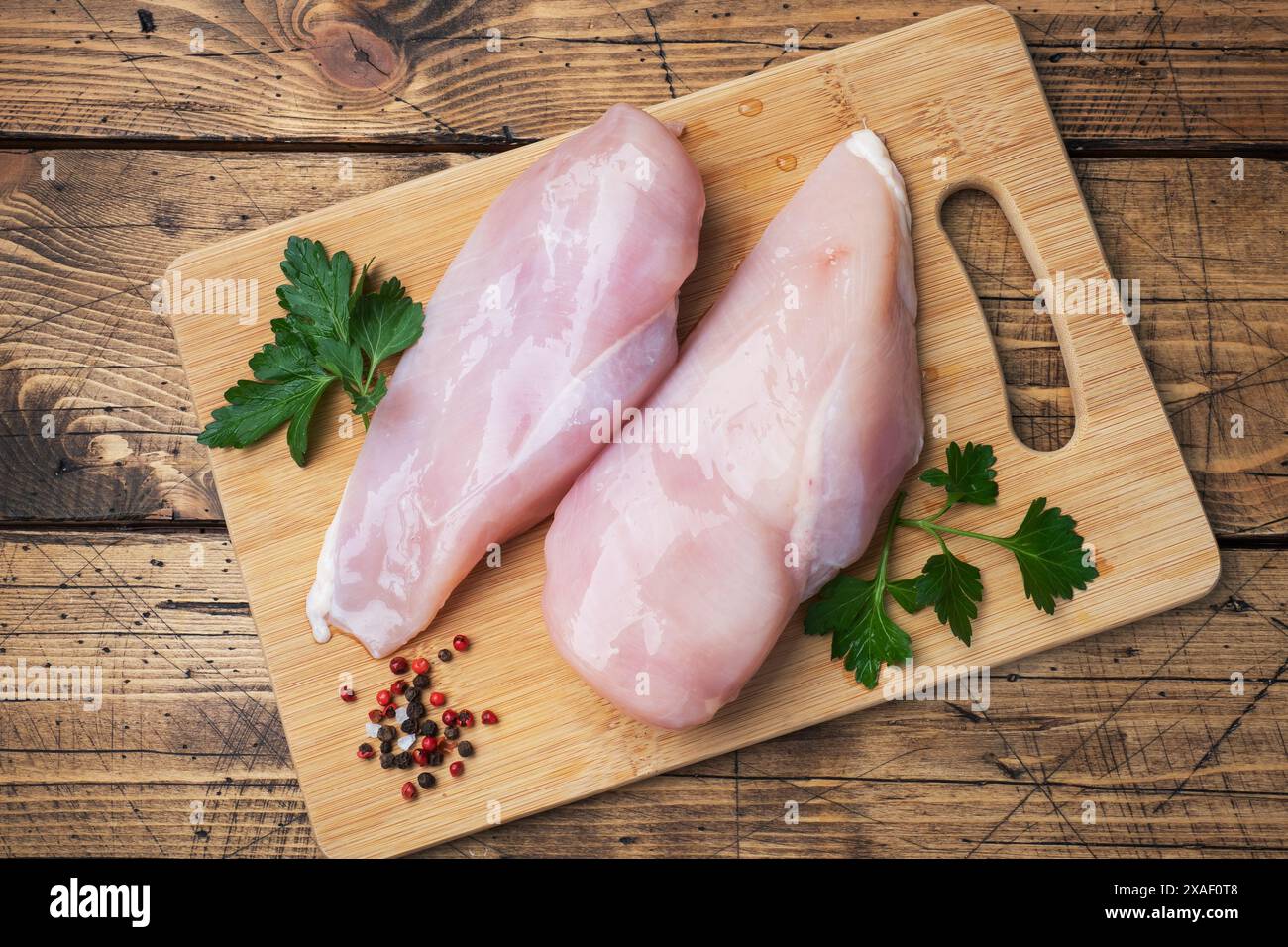 Filet de poitrine de poulet cru sur une planche à découper en bois. Vue de dessus de fond rustique en bois Banque D'Images Filet de poitrine de poulet cru sur une planche à découper en bois. Vue de dessus de fond rustique en bois Banque D'Images