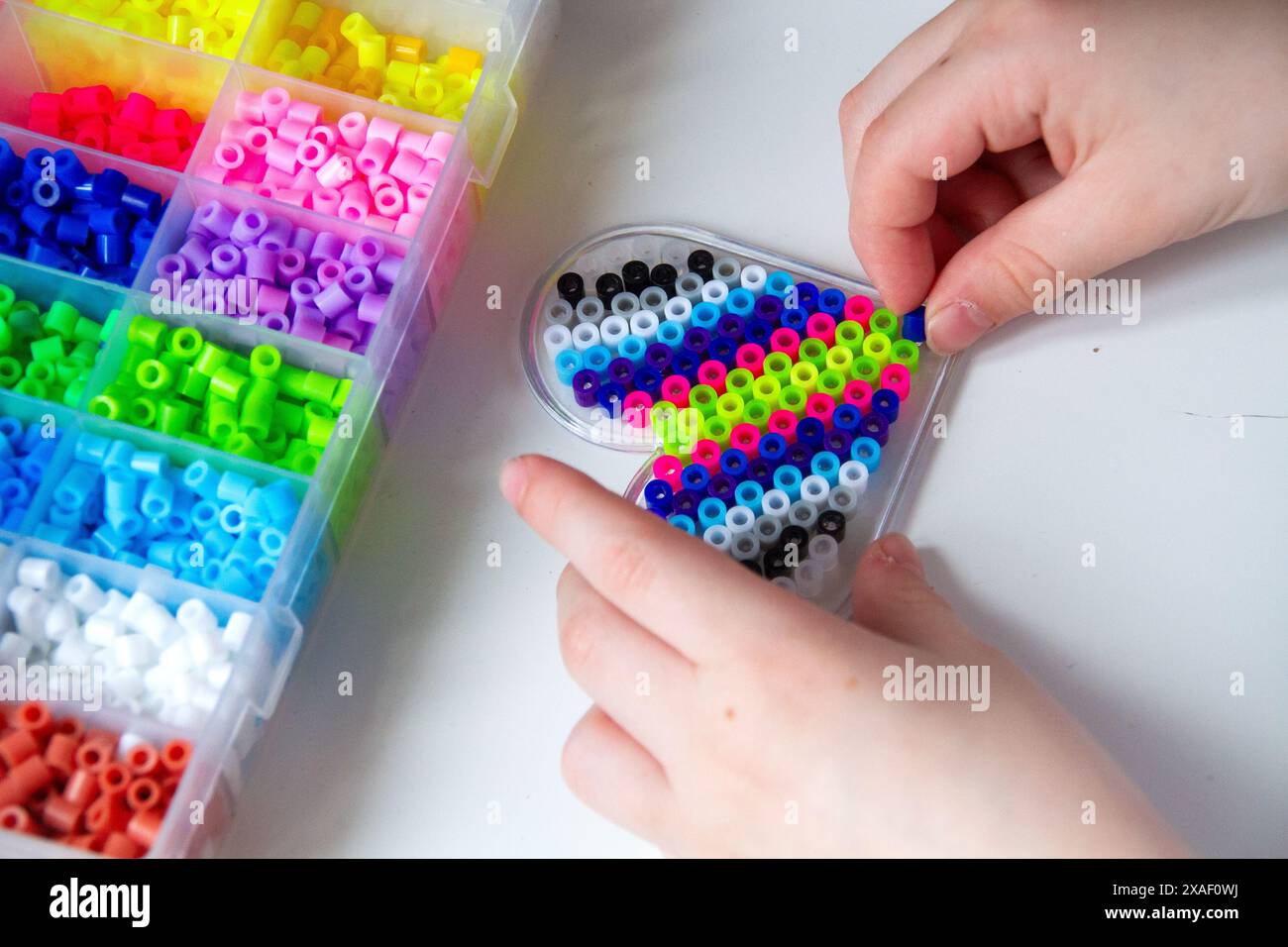 Vue de dessus aux mains d'un enfant qui crée un cœur avec des perles en plastique à partir de perles de différentes couleurs et boîte avec des perles Banque D'Images