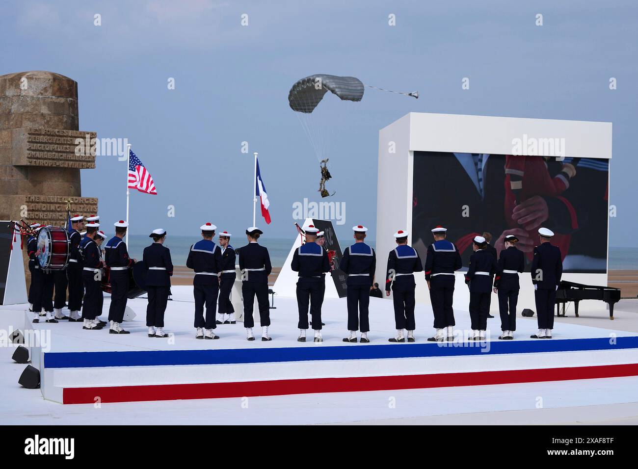 Normandie, France. 06 juin 2024. Un parachutiste (C) arrive alors qu'une bande de musiciens de la Marine française joue lors de la cérémonie commémorative internationale à Omaha Beach marquant le 80e anniversaire du débarquement allié du jour J de la seconde Guerre mondiale en Normandie, à Saint-Laurent-sur-mer, dans le nord-ouest de la France, le 6 juin 2024Photographie de l'Ambassade des États-Unis France/UPI. Crédit : UPI/Alamy Live News Banque D'Images