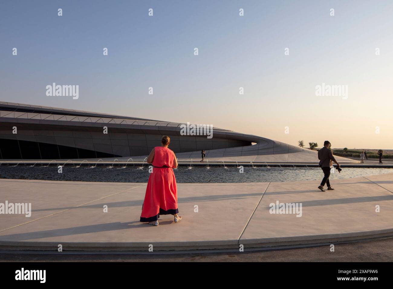 Les gens marchant passaient devant le grand étang à l'extérieur du bâtiment principal. Siège social de BEEAH, Sharjah, Émirats arabes Unis. Architecte : Zaha Hadid Architects, 2 Banque D'Images