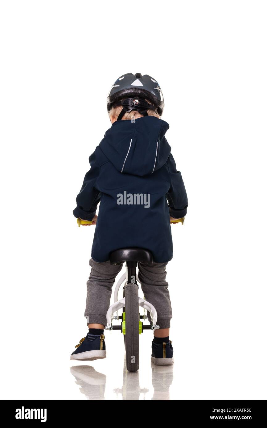 Vue arrière d'un tout-petit conduisant un vélo d'équilibre avec un casque, favorisant la sécurité des enfants et une activité saine. Banque D'Images