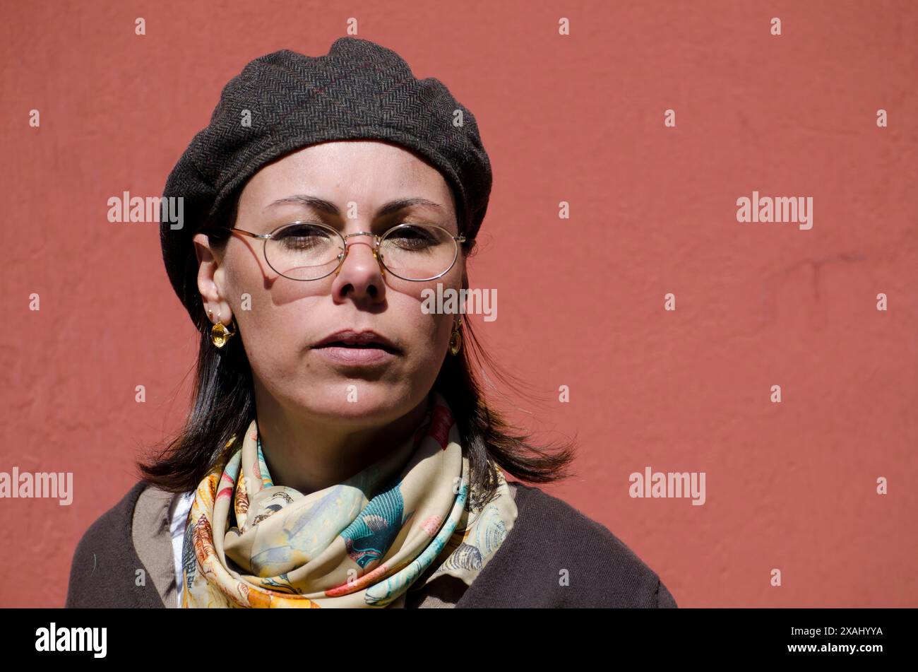 Artiste femme avec chapeau plat et lunettes et écharpe sur fond rouge dans un jour ensoleillé en Suisse Banque D'Images