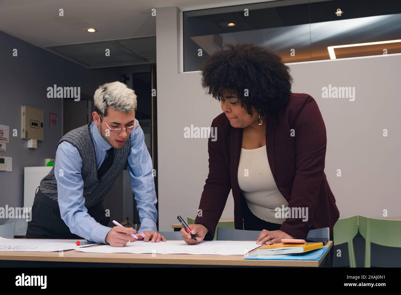Deux jeunes femmes et hommes travaillent ensemble sur un projet qu'ils parlent et prennent des notes sur un papier. Ils écrivent sur une table avec des stylos Banque D'Images