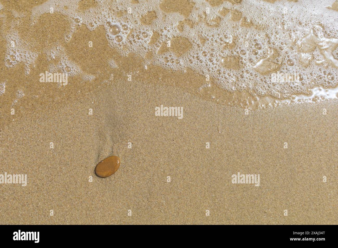 gros plan photo plate d'une surface de plage de sable humide avec marée et petite pierre brune Banque D'Images