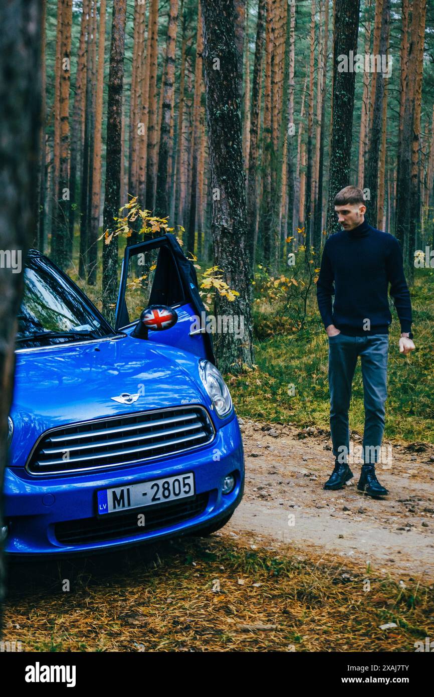 Hommes avec hommes bleus Mini Cooper Country et parapluie bleu le jour nuageux dans la forêt de pins. Banque D'Images