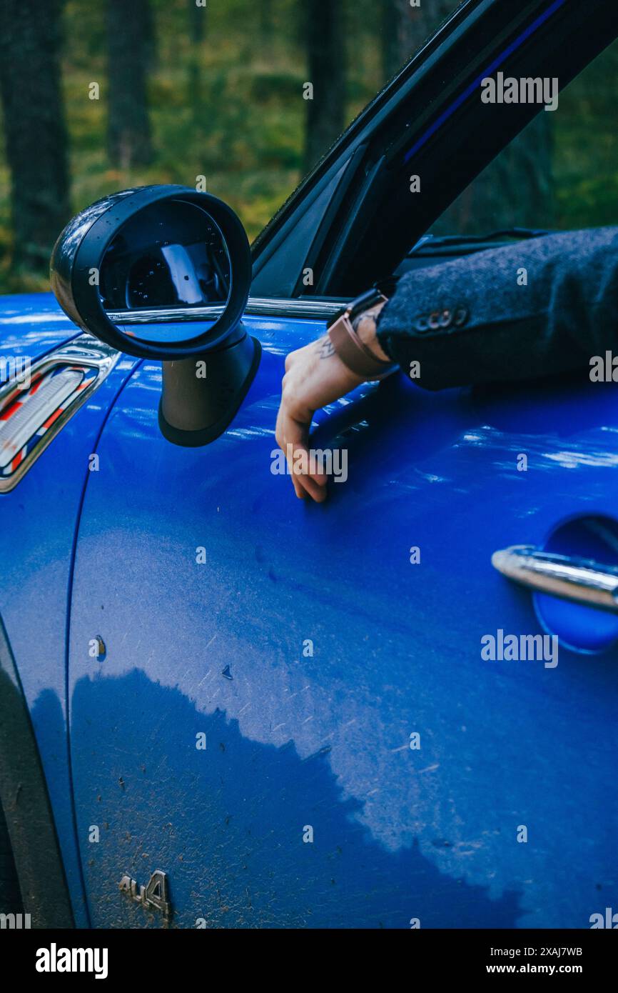 Hommes avec hommes bleus Mini Cooper Country et parapluie bleu le jour nuageux dans la forêt de pins. Banque D'Images