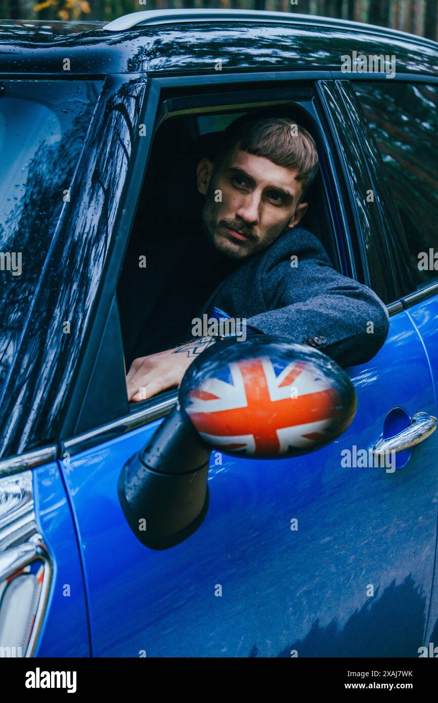 Hommes avec hommes bleus Mini Cooper Country et parapluie bleu le jour nuageux dans la forêt de pins. Banque D'Images