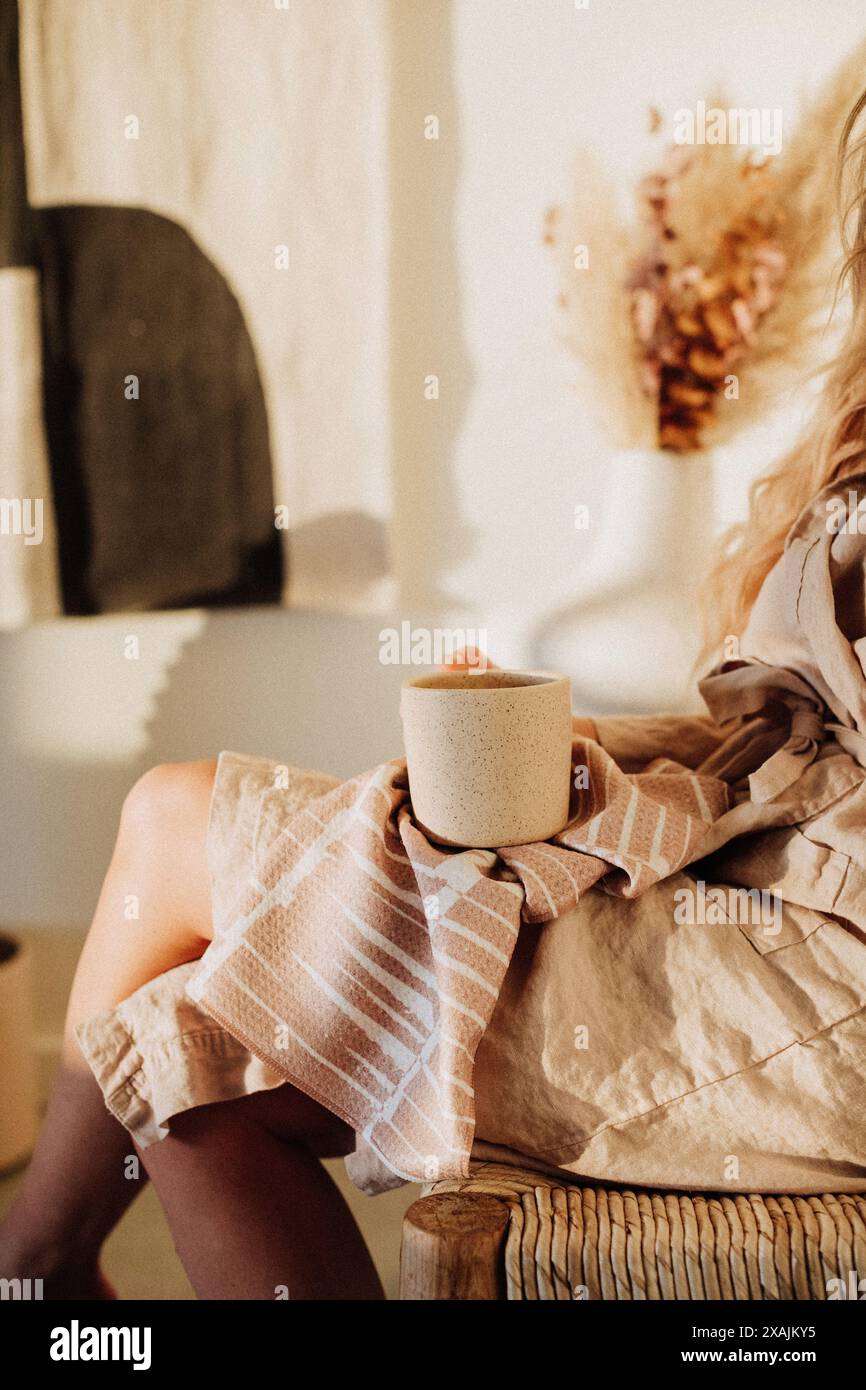 Femme tenant une tasse et un chiffon, assise dans un cadre confortable Banque D'Images