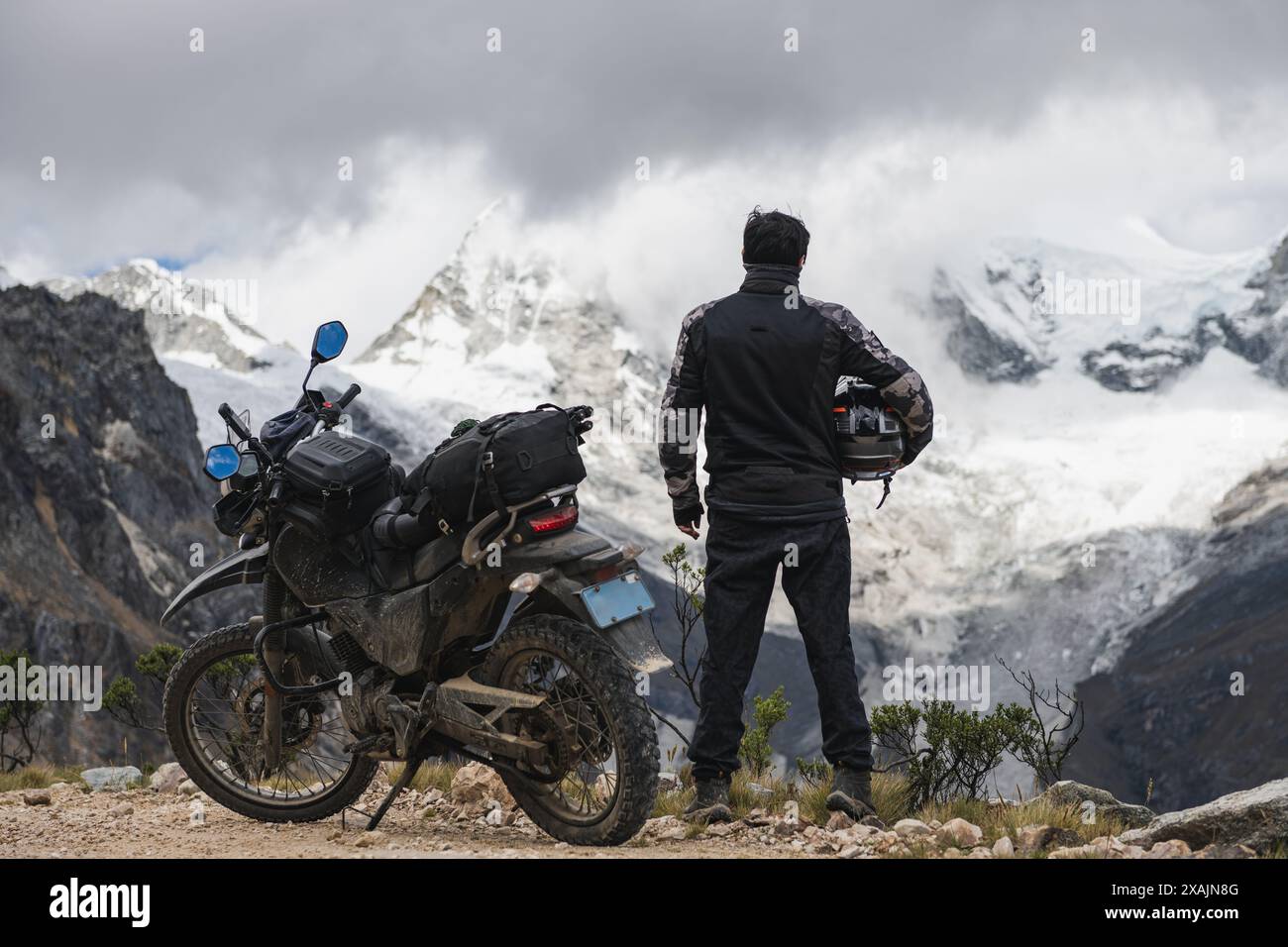 Homme avec une moto d'aventure devant une montagne enneigée. Banque D'Images