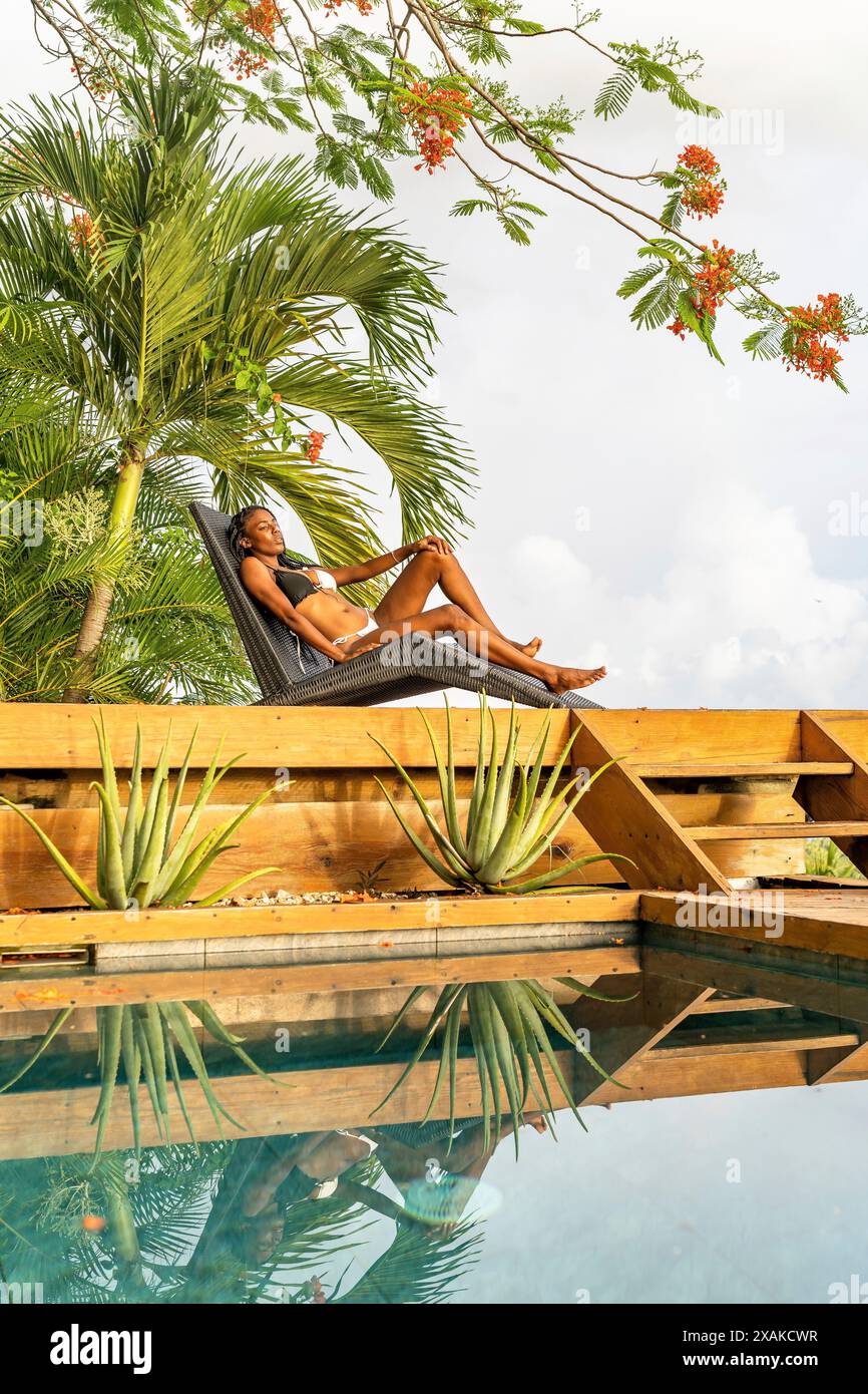 Amérique du Nord, Caraïbes, île d'Hispaniola, République dominicaine, péninsule de Samana, Sanchez, Jardines la Loma, jolie femme à la peau foncée allongée sur une chaise longue à côté de la piscine Banque D'Images