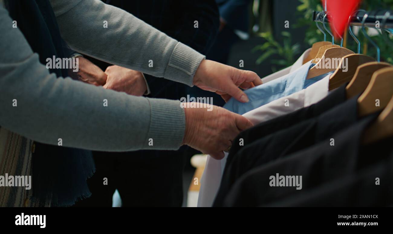 Femme senior cherchant des vêtements pour son mari, à la recherche de costumes élégants sur cintres au grand magasin. Couple de personnes âgées magasinant pour la nouvelle collection de mode au showroom. Caméra B. Banque D'Images