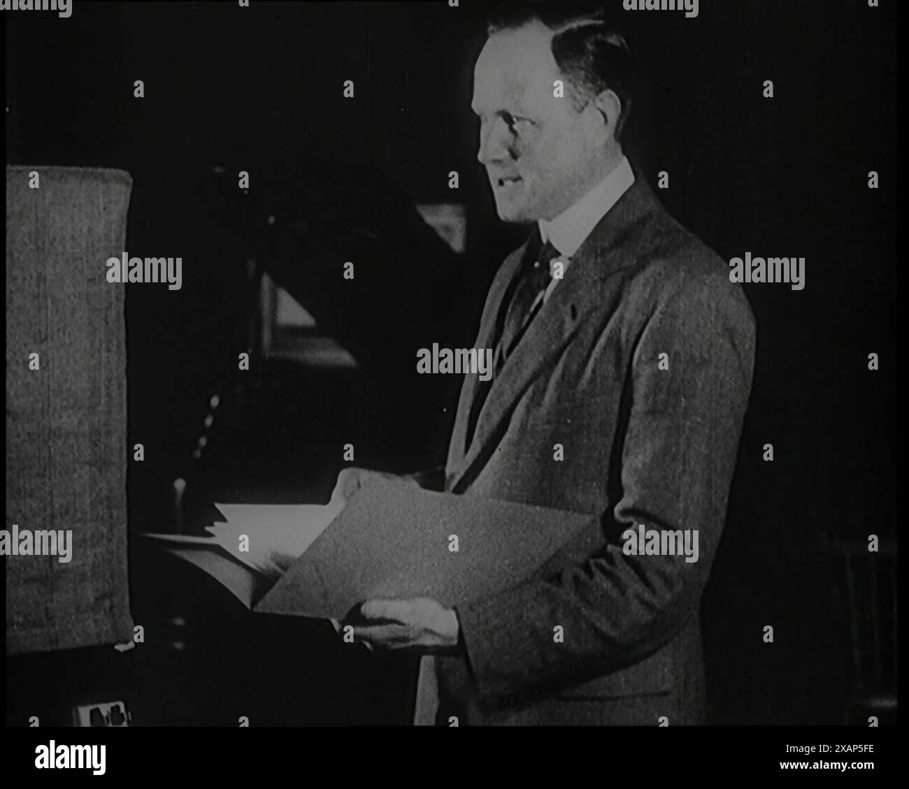 A Man Reading from a Book for the British Broadcasting Corporation, 1922. De "Time to Remember - Sitting Still and Going Slowly", 1922 (bobine 4) ; un examen des événements de 1922, y compris les troubles irlandais, la guerre entre la Grèce et la Turquie et les développements dans l'aviation et la radio. Banque D'Images