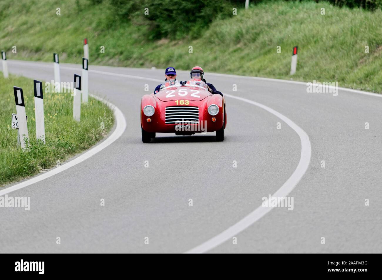 Voiture de course vintage rouge dans la courbe d'une route de campagne à travers des paysages verts, avec deux pilotes, course, voiture classique, course de voiture, mille Miglia, 1000 Miglia Banque D'Images