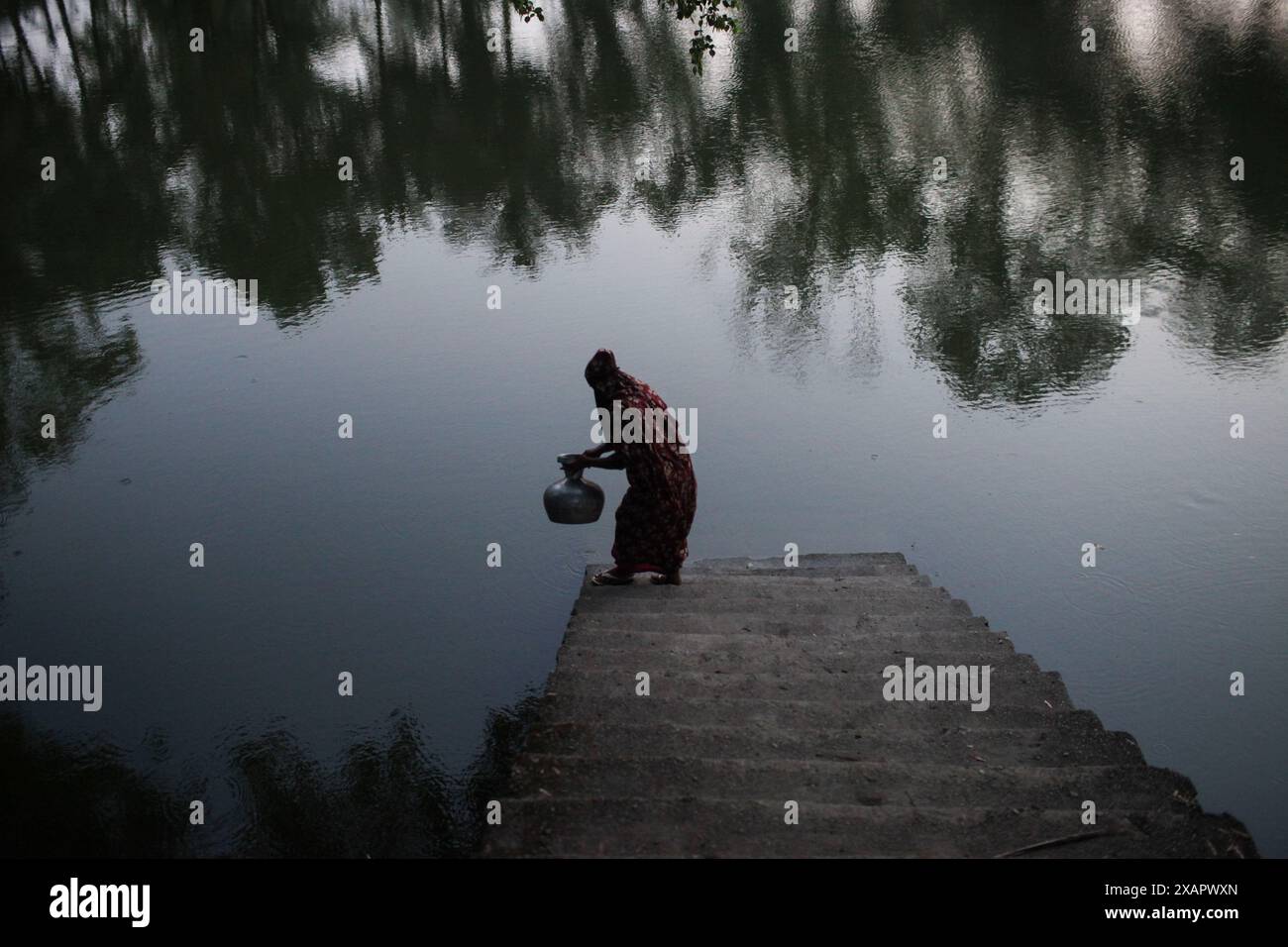 8 juin 2024, Dhaka, Dhaka, BANGLADESH : une femme bangladaise collecte de l'eau potable à partir d'une source d'eau douce, marchant un long chemin pour recueillir de l'eau potable dans la zone côtière de Khulna, au Bangladesh. Selon une étude de l’American Geophysical Union, l’élévation du niveau de la mer, qui affecte la disponibilité de l’eau potable, entraînera la migration d’environ 1,3 millions de personnes à travers le pays d’ici 2050. Une combinaison d'inondations dues aux marées, d'inondations dues aux ondes de tempête et d'intrusion d'eau salée entraîne une augmentation de la salinité dans les eaux souterraines et les étangs d'eau douce, causant une augmentation de la salinité du dr Banque D'Images