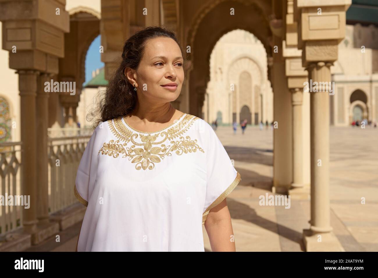 Une femme confiante en vêtements blancs traditionnels se tient dans un cadre architectural historique magnifiquement sculpté sous la lumière du soleil. Elle apparaît conte Banque D'Images