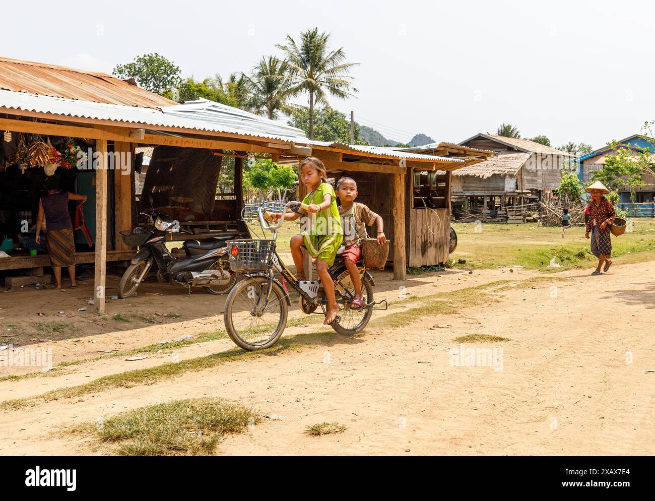 Enfants à vélo sur la route de terre, village de Nong Ping, Laos Banque D'Images