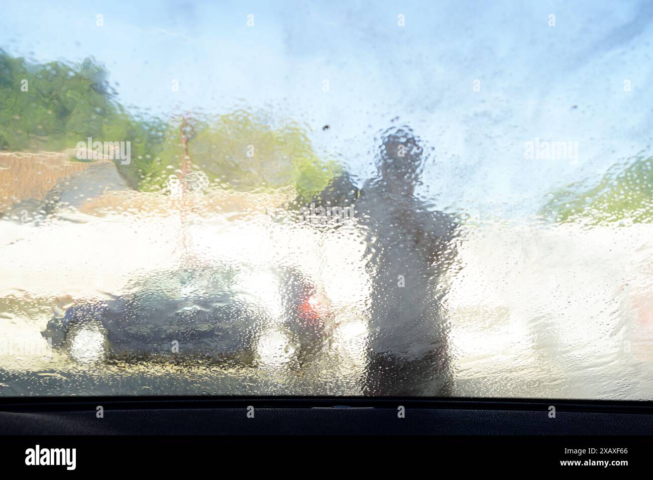 Lavage de la vitre avant avec un pistolet de lavage - un jet d'eau coulant d'un pistolet de lavage à haute pression, vue de l'intérieur de la voiture. Banque D'Images