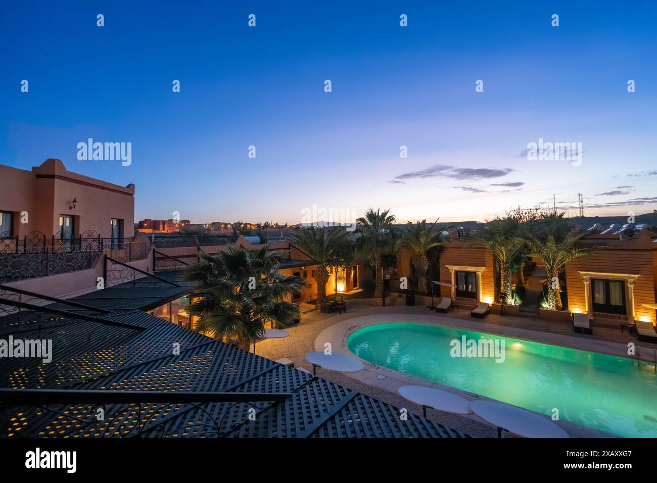 Ouarzazate, Maroc - 19 mars 2024 : le crépuscule tombe sur la piscine tranquille de l'hôtel, reflétant l'architecture marocaine traditionnelle. Banque D'Images