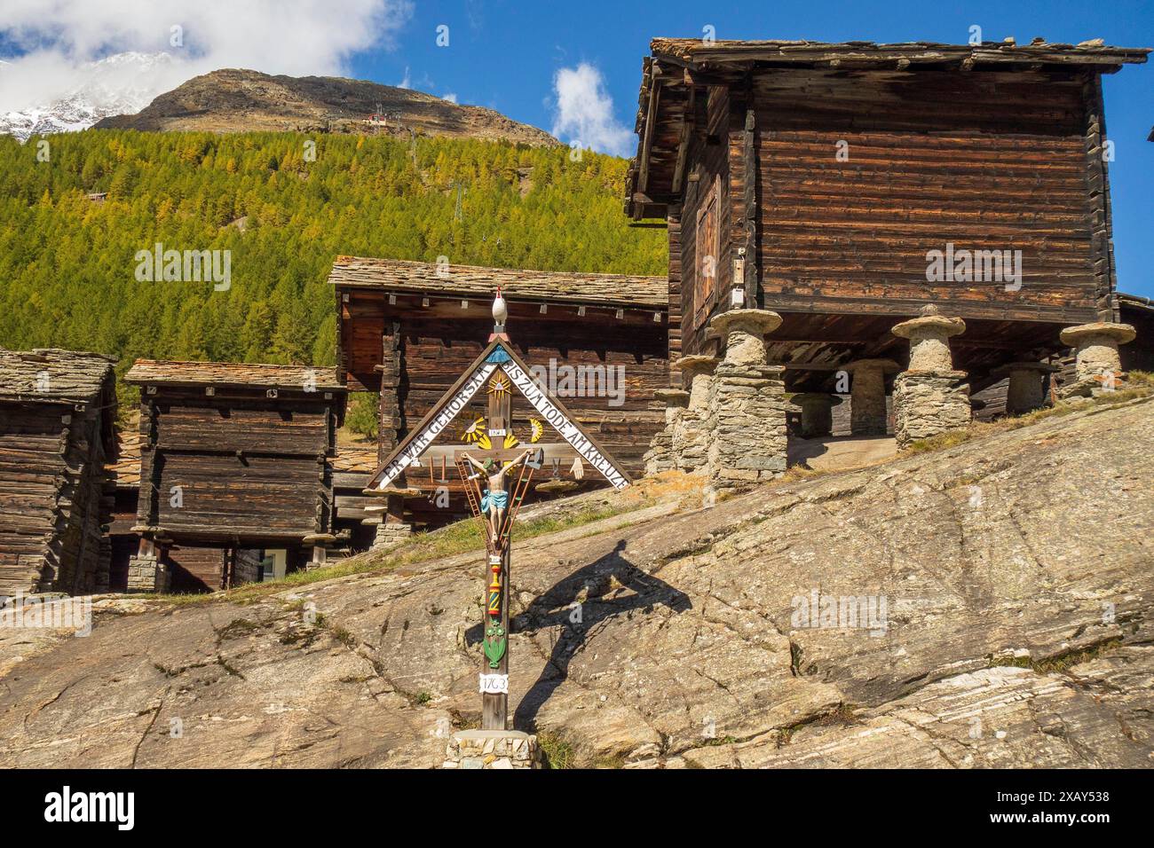 Cabanes en bois sombre sur des fondations en pierre et une grande croix sur fond de montagne, Saas Fee, Suisse Banque D'Images