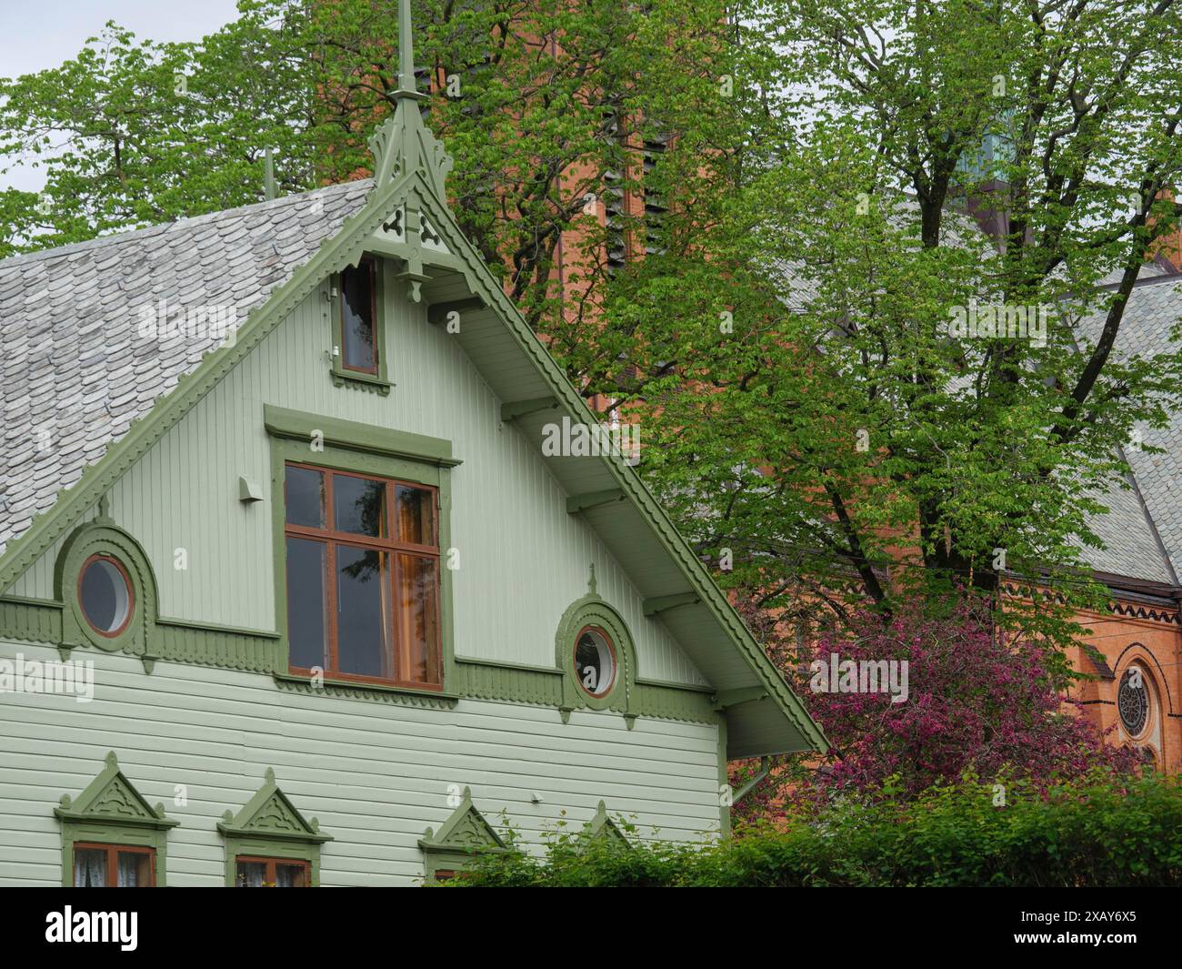 Maison verte décorative devant un clocher d'église et arbres en fleurs au printemps, Haugesund, norvège Banque D'Images