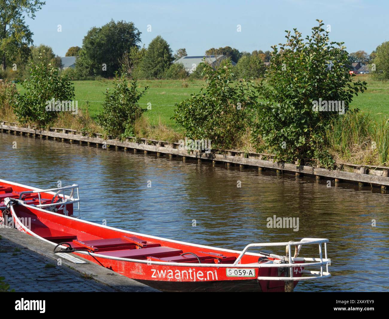 Un bateau rouge se trouve sur la rive d'un canal, entouré de champs verdoyants et d'arbres, à giethoorn, pays-Bas Banque D'Images