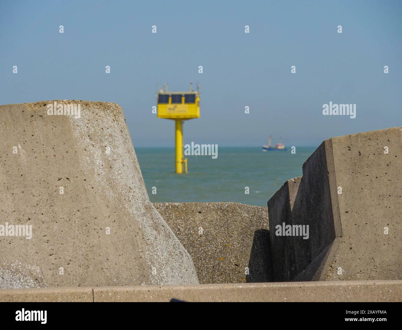 Côte avec de grands blocs de béton et une tour jaune dans la mer, plus loin vous pouvez voir un bateau, ostende, Belgique Banque D'Images