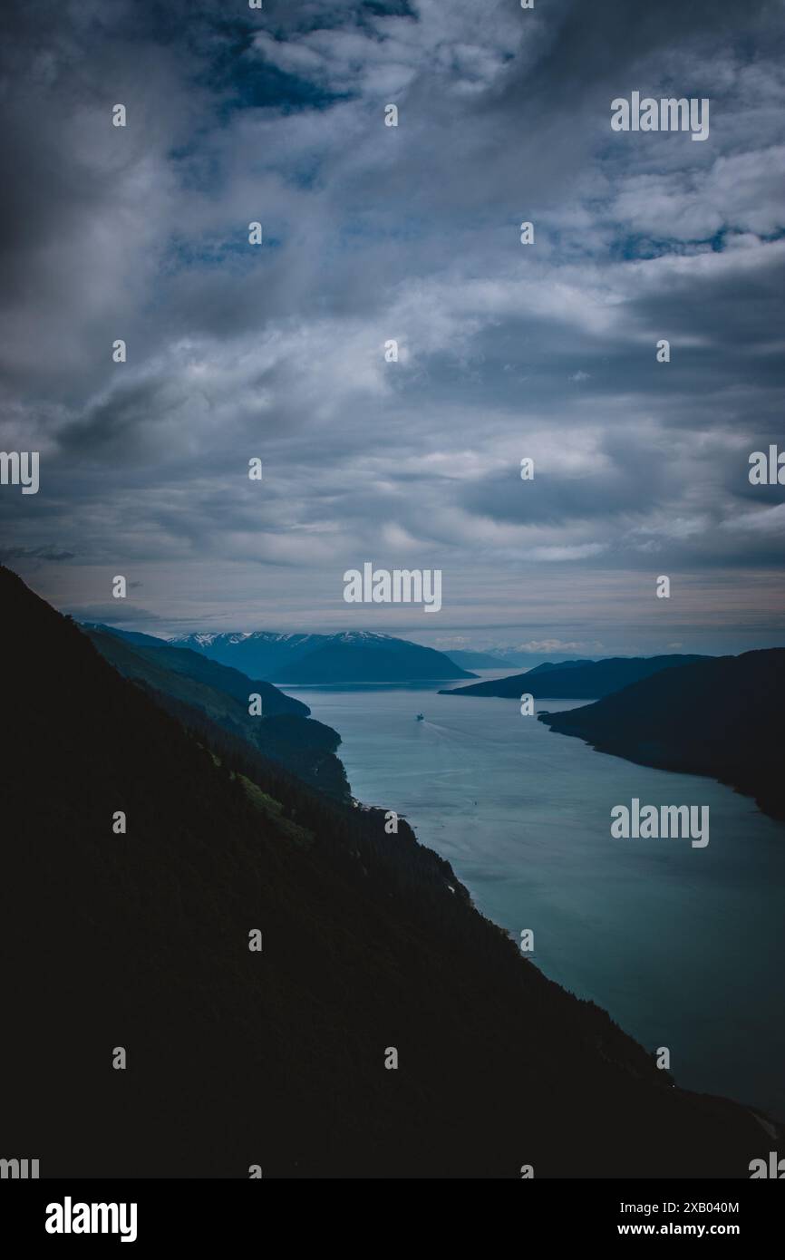 Capturez la beauté enchanteresse des fjords de l'Alaska avec des nuages spectaculaires, des eaux sereines et des montagnes escarpées, parfaites pour évoquer un sentiment de tranquillité Banque D'Images