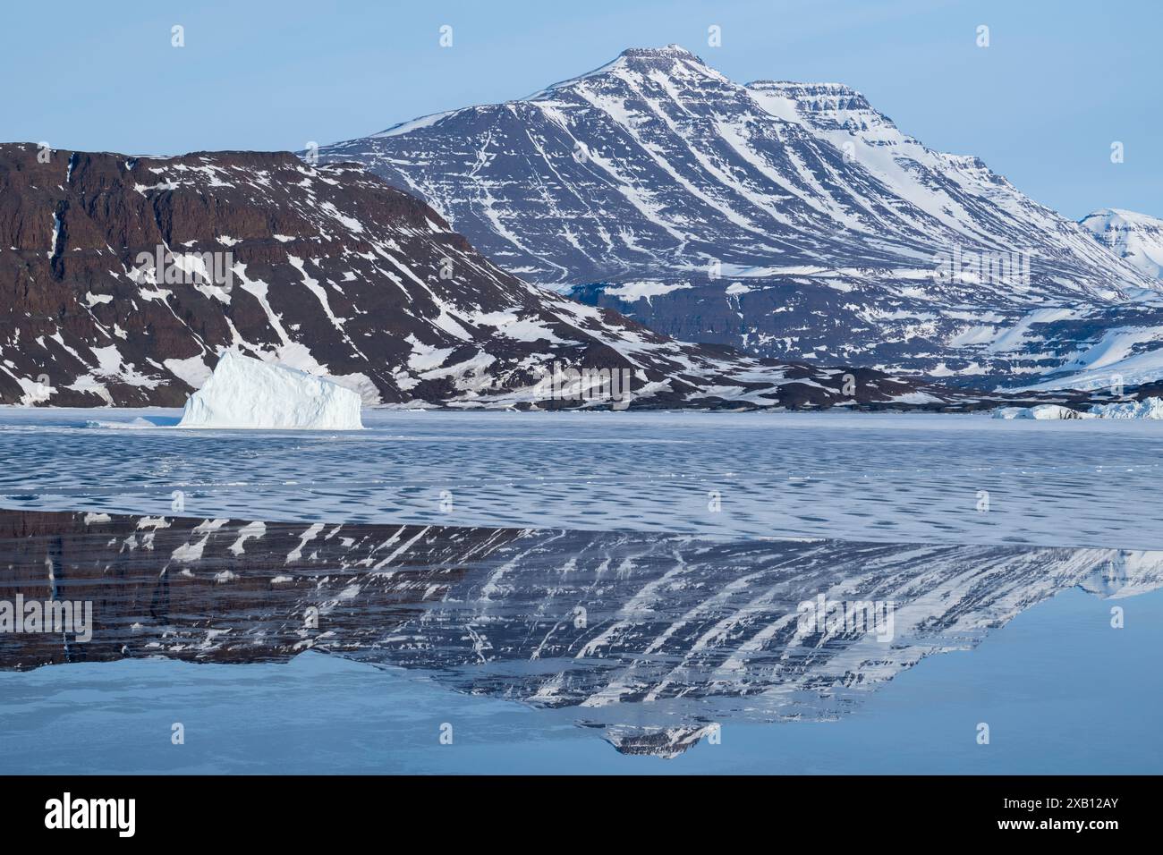 Groenland oriental, Côte de Blosseville. Tôt le matin, reflets gelés de fjord, avec iceberg. Banque D'Images
