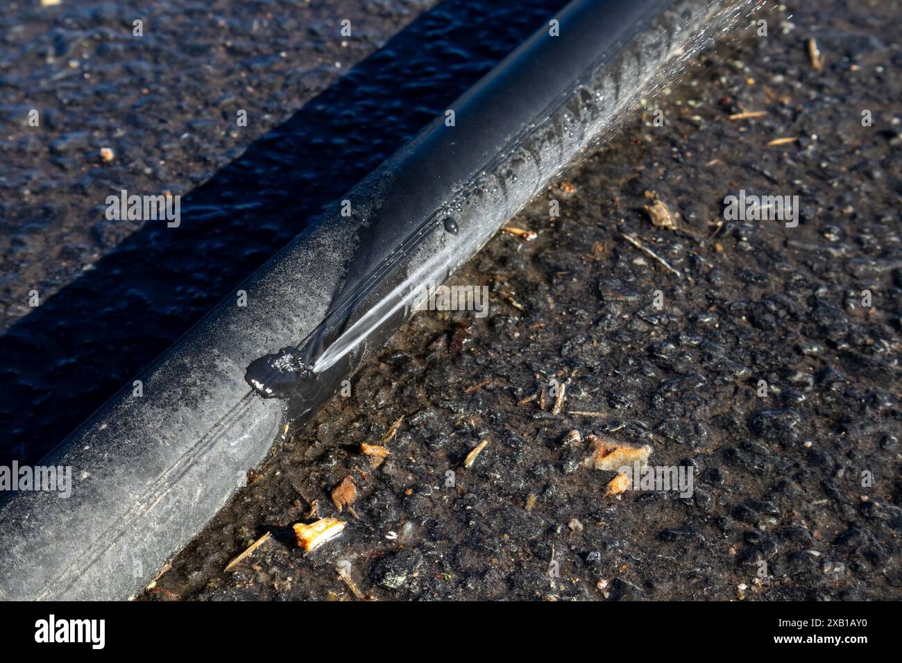 Fuite de tuyau d'eau en polyéthylène noir sur le sol à l'extérieur Banque D'Images