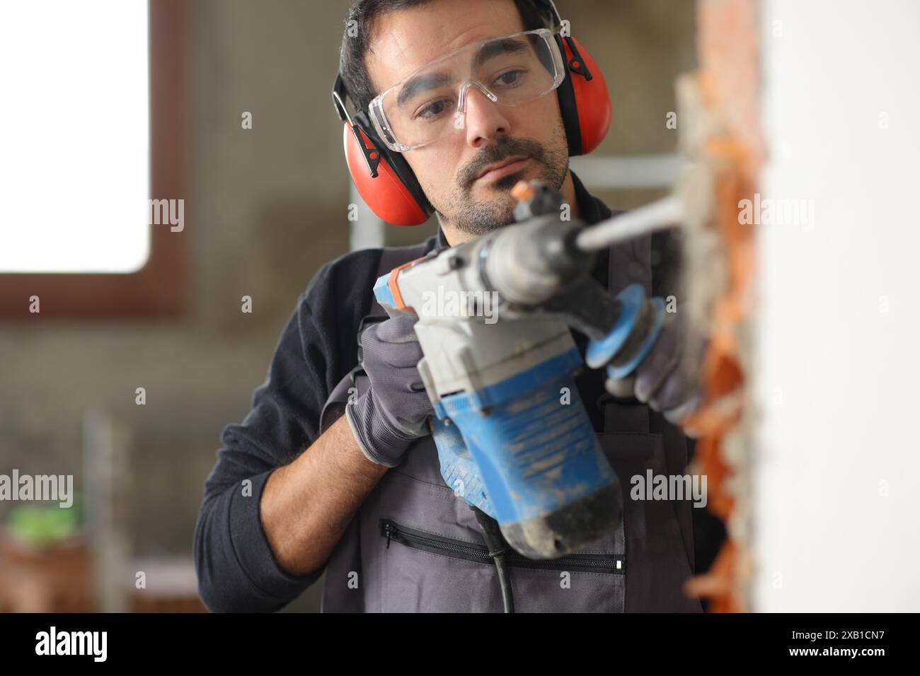 Travailleur de la construction détruit le mur à l'aide d'un marteau rotatif dans une maison en cours de réforme Banque D'Images