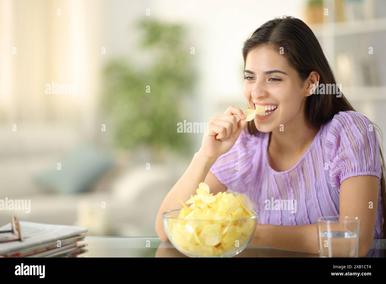 Femme heureuse riant et mangeant des chips seule à la maison Banque D'Images